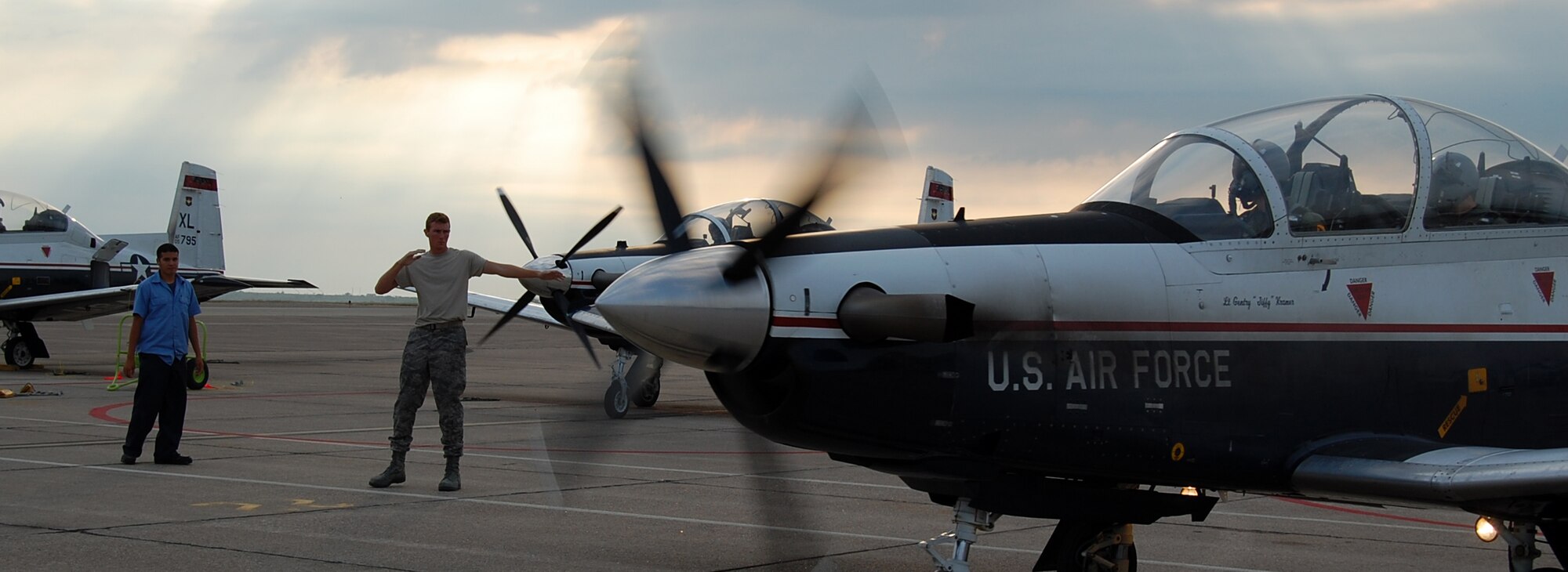 LAUGHLIN AIR FORCE BASE, Texas—2nd Lt. Kevin Hawkins, 47th Operation Support Squadron, marshals a T-6 Texan II as civilian crew chief Eric Martinez, T-6 A-Cell, watches. Lieutenant Hawkins is one of the many United States Air Force Academy graduates stationed at Laughlin who have been tasked to perform various jobs while waiting for their Specialized Undergraduate Pilot Training to start. He is currently acting as a T-6 A-Cell crew chief for his casual status job. (U.S. Air Force photo by 2nd Lt. Cody Chiles)