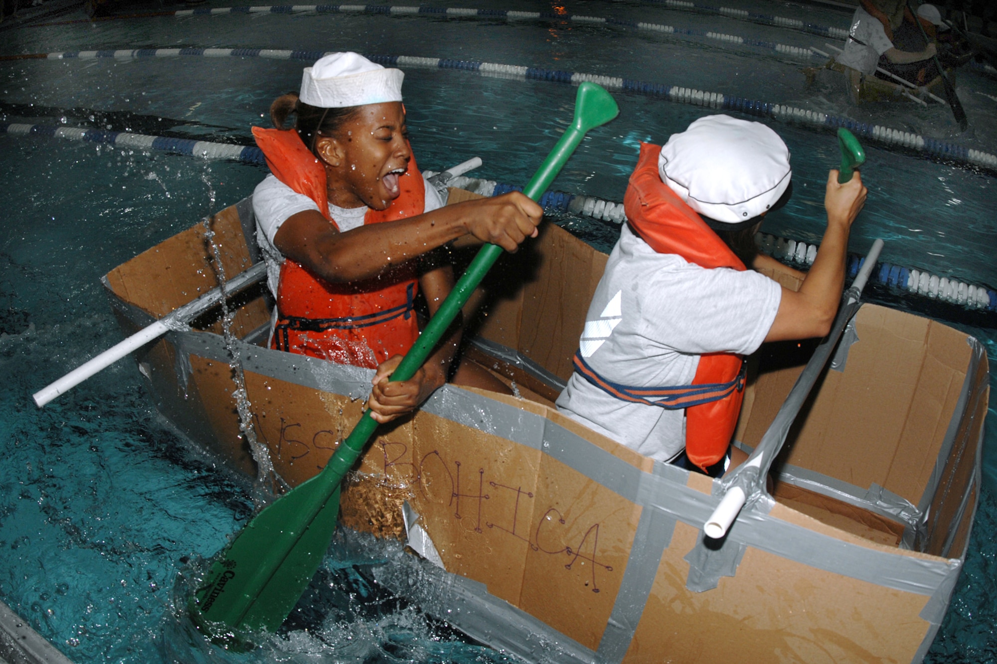 Airman 1st Class Eugenia Heart and Staff Sgt. Kelly Bender, 55th Maintenance Squadron, paddle through the rough waters of the Offutt Field House indoor lap pool during the Card Board Boat Race challenge for Wingman Day on September 25. (U.S. Air Force Photo By Charles Haymond)