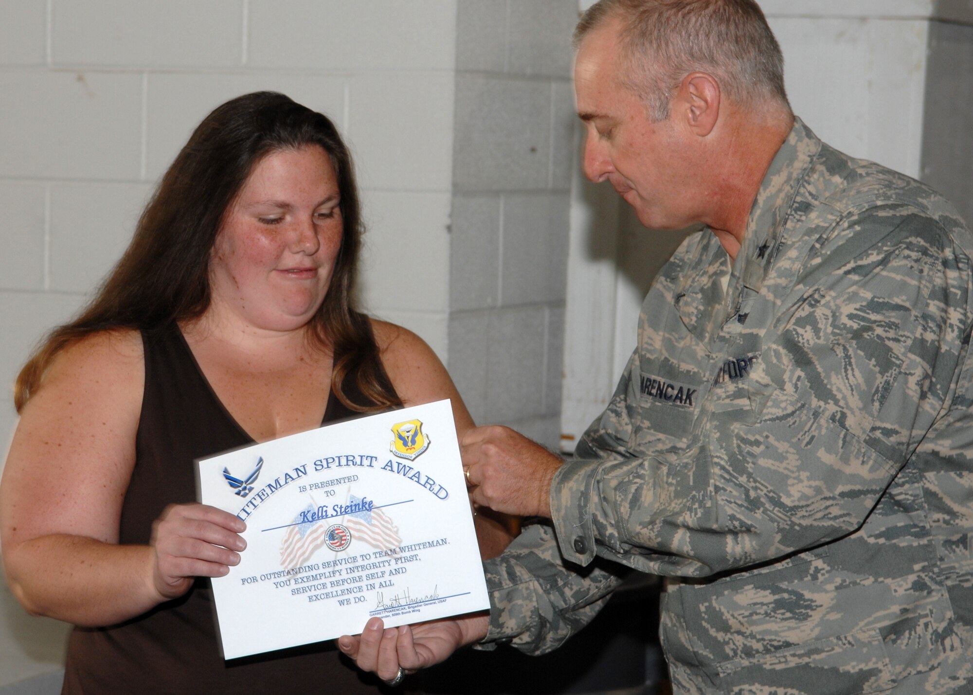 WHITEMAN AIR FORCE BASE, Mo., -- Brig. Gen. Garrett Harencak, 509th Bomb Wing commander, presentes Kelli Steinke, wife of Staff. Sgt. Kevin Steinke, 509th Civil Engineering Squadron, with the Whiteman Spirit Award and his commander's coin Sept. 2. (U.S. Air Force courtesy photo)