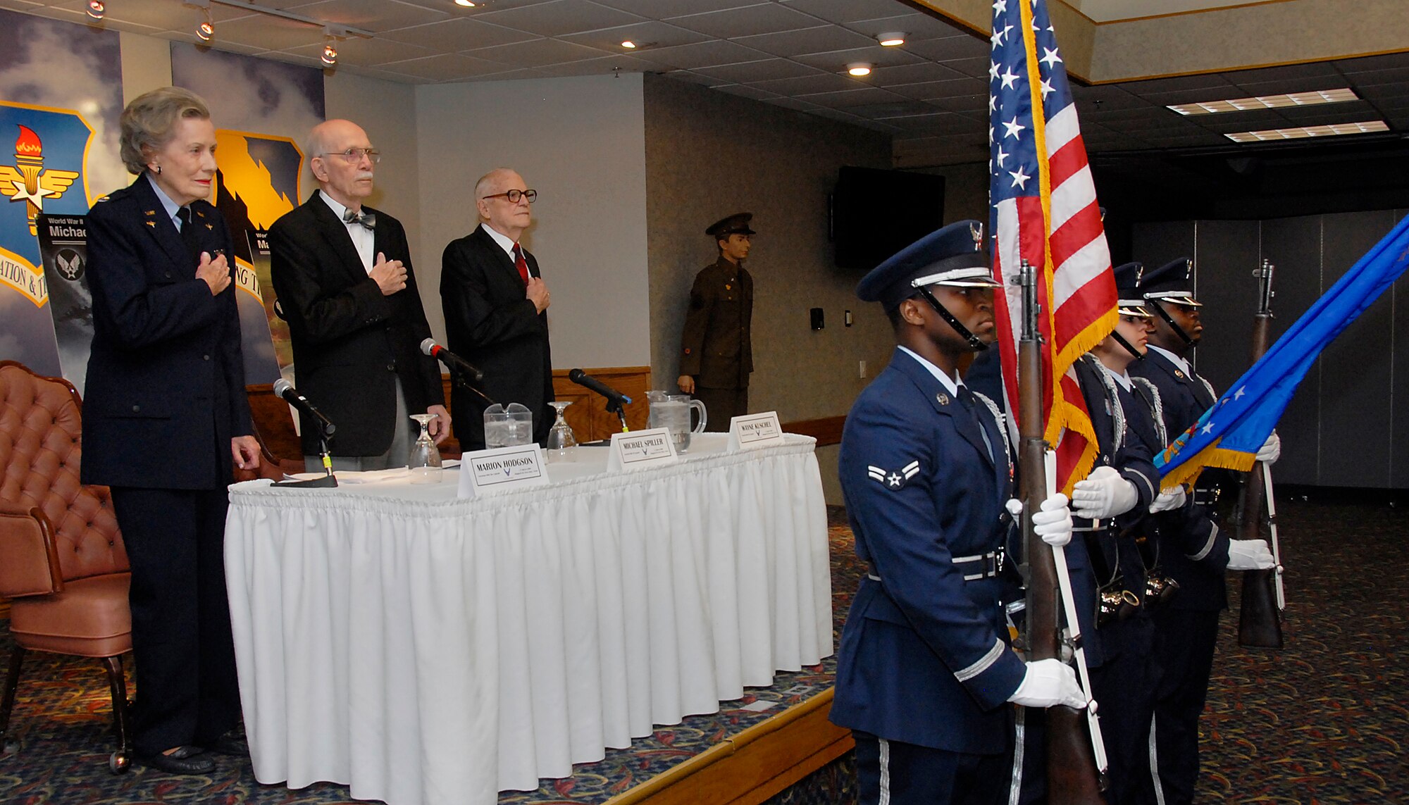 World War II pilots (from left to right on stage) Marion Stegeman Hodgson, Michael Spiller and Wayne Kuschel pay respect to the national anthem March 31 during a "Lunch with the Legends" luncheon at the Sheppard Club. The three shared their experiences working in and with the Army Air Corps during the second world war. (U.S. Air Force photo/Mike Litteken)