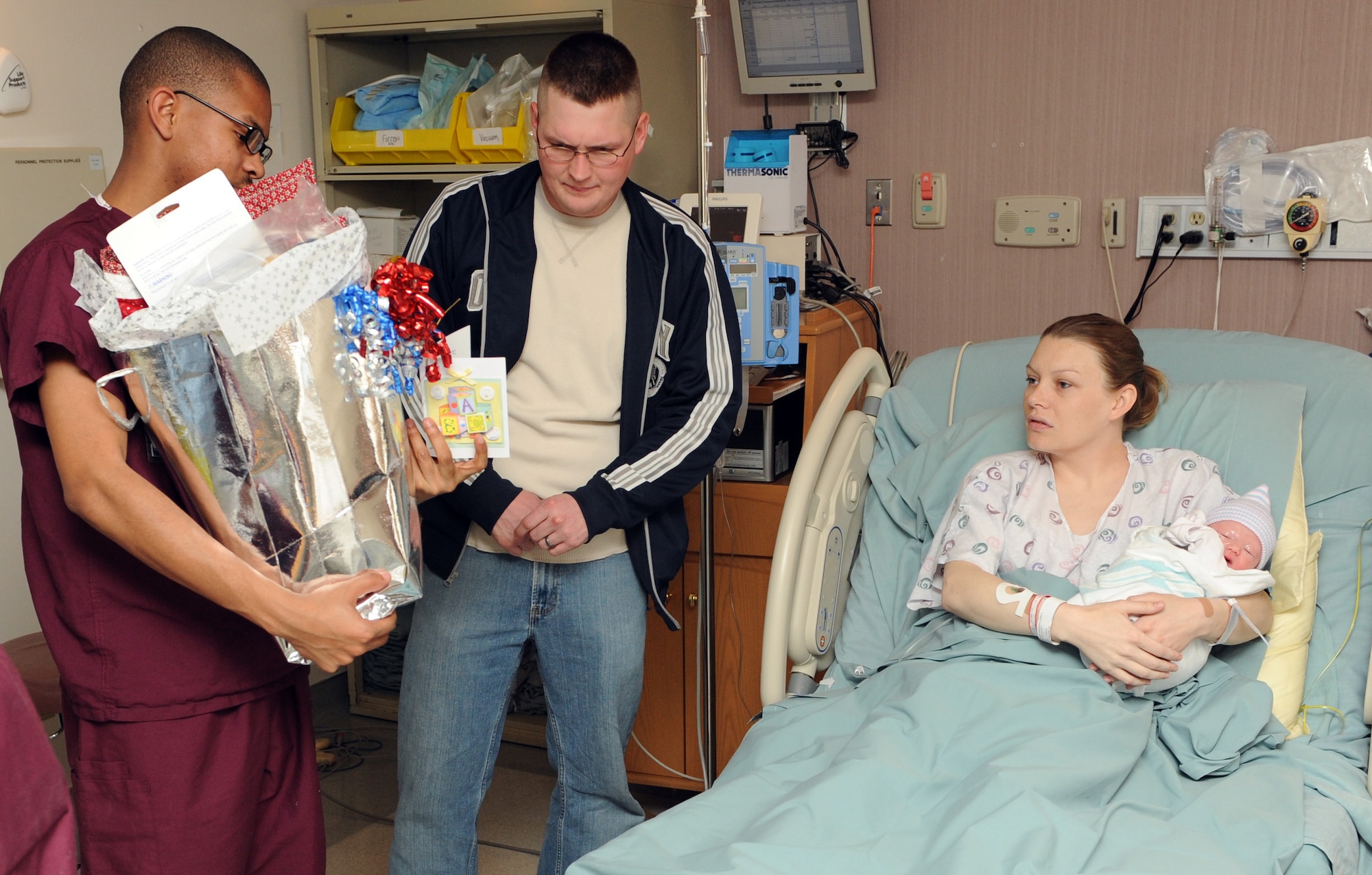 MOUNTAIN HOME AIR FORCE BASE, Idaho - Left, Airman 1st Class Aaron Porter, 366th Surgical Operations Squadron medical technician, presents new parents, Matthew and Dena Norwood and their baby girl, Kirsten Charolette Norwood, with the 1,000th bundle from Hammonds Baby Bundles at the base hospital March 24. Each baby bundle contains a handmade quilt and card made by base and local volunteers along with clothing, a stuffed animal and hat. Every baby born at the base hospital receives a bundle with each one numbered and tracked. (U.S. Air Force photo by Airman 1st Class Debbie Lockhart)