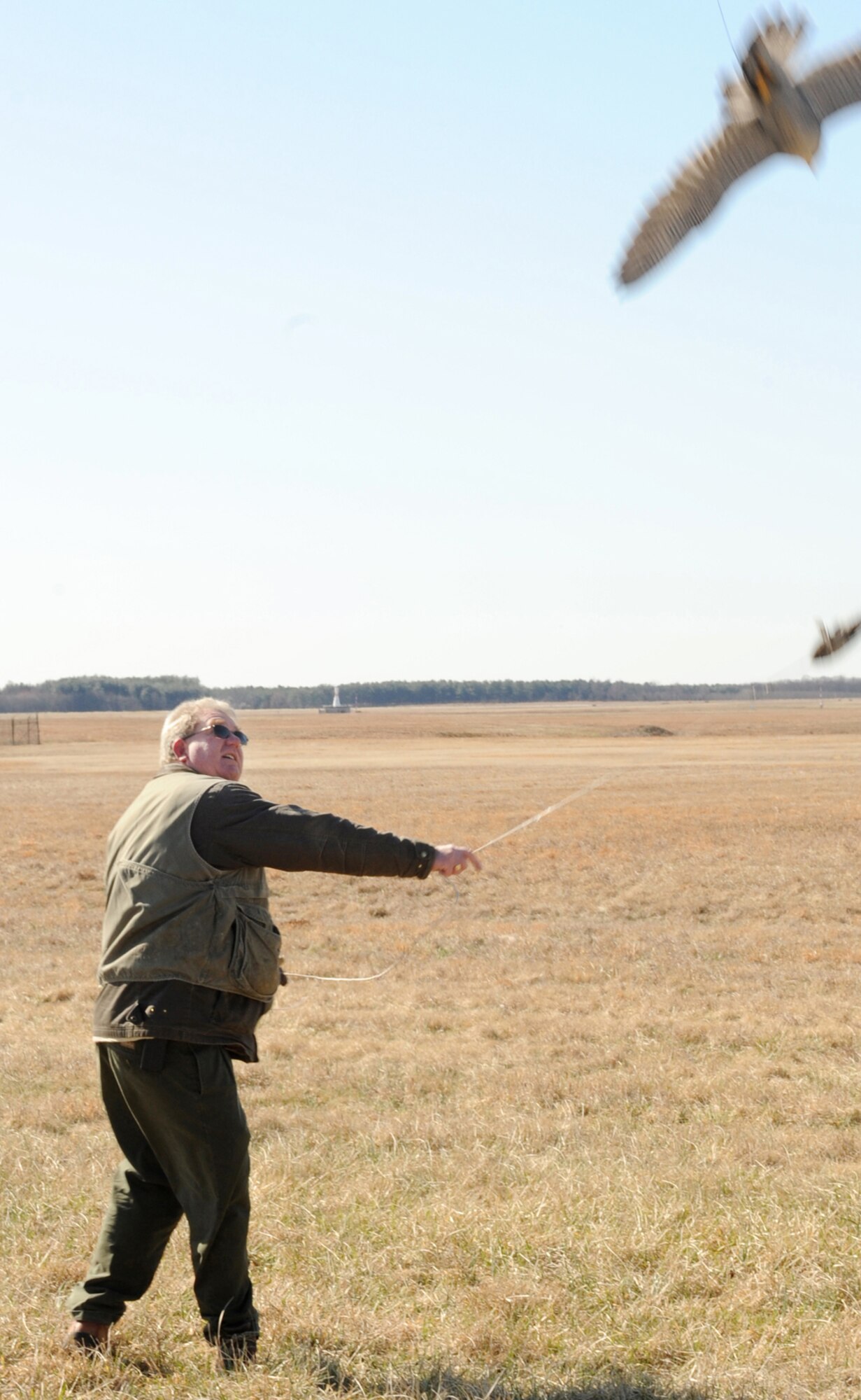 Falconer Andrew Barnes takes Nantucket through a work out by twirling a rope with a bird-like target on the flightline March 23. The training flight takes place during Nantucket’s normal patrol slot when there are no birds in the vicinity. The falcons are a natural deterrent to all birds local to McGuire except sparrows, which are too small and cause less than one percent damage to McGuire equipment, and turkey vultures, which are too large of a bird for the falcons to take on. Unlike pyrotechnics and noises, which birds become accustomed to, the falcon is a real and natural predator. (U.S. Air Force photo/Wayne Russell)