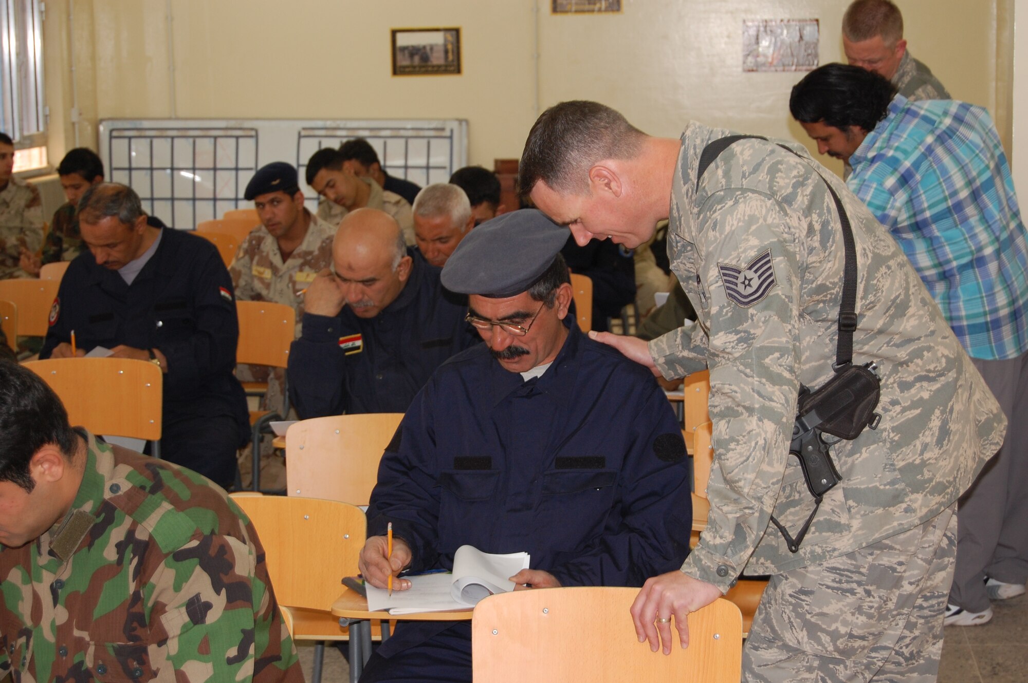 Tech. Sgt. Mike Higby, 821st Expeditionary Training Squadron Iraqi warrant officer professional development course instructor, helps one of his Iraqi students with a question during their final test March 28. Twenty-nine Iraqi warrant officers completed the seven-day course where they were taught lessons on discipline, leader influence, teamwork and development, ethics and values, Law of Armed Conflict and problem solving. Sergeant Higby is deployed from Kapaun Air Base, Germany, and is a native of Anchorage, Alaska. (U.S. Air Force photo by Staff Sgt. Tim Beckham)