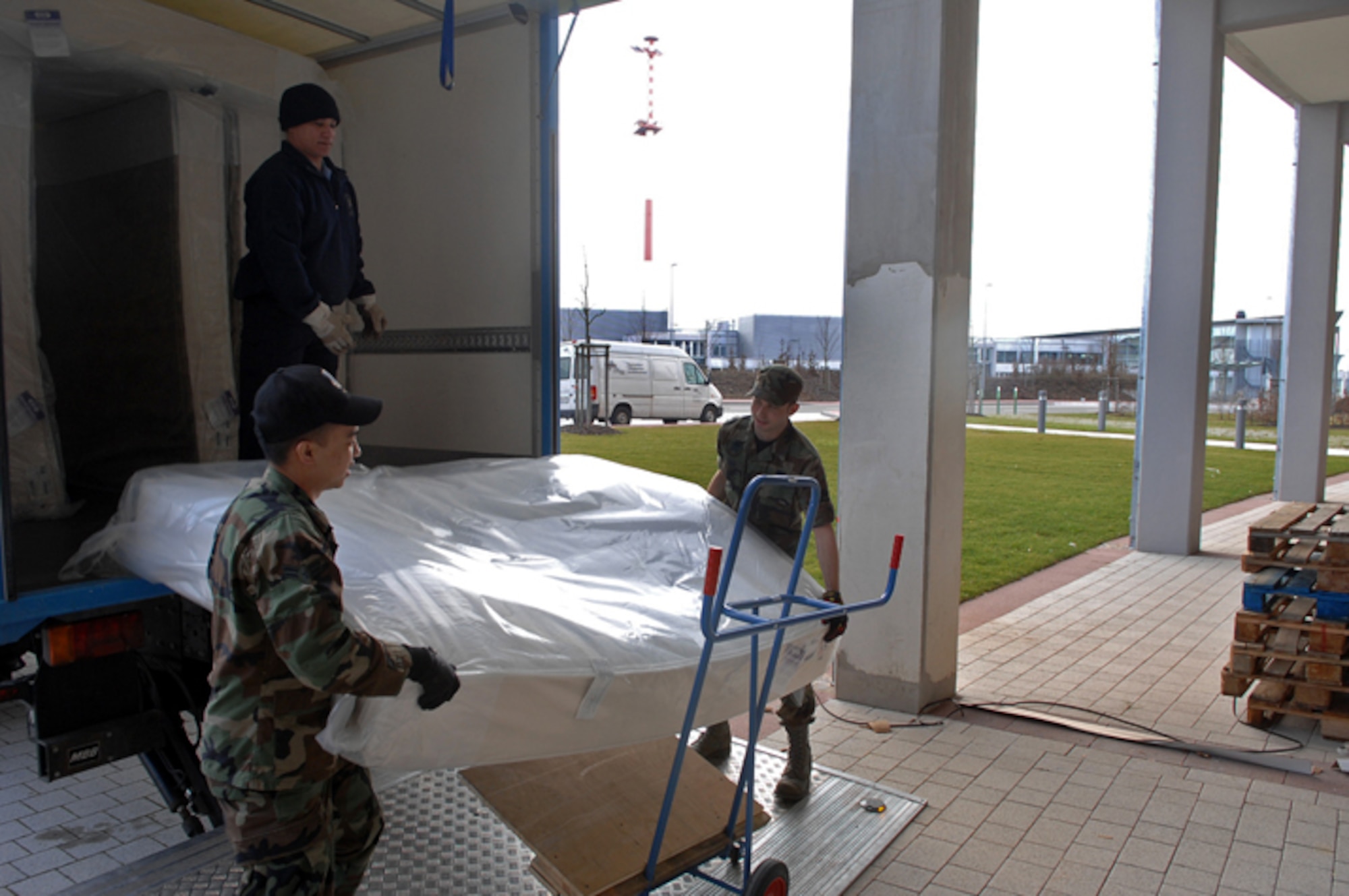 Hector Martinez, Air Force Inns Material Handler, Airmen 1st Class Byron Sy(left) and Allen Long, 435th Services Squadron, offload mattresses for the new visitor quarters at the Kaiserslautern Military Community Center on Ramstein Air Base. The eight-story, 350-room visiting quarters facility will be one of the first areas to open as part of a $170 million project that will offer approximately 844,000 square feet of lodging, shopping and entertainment under one roof. (U.S. Air Force photo by Airman 1st Class Tony Ritter)
