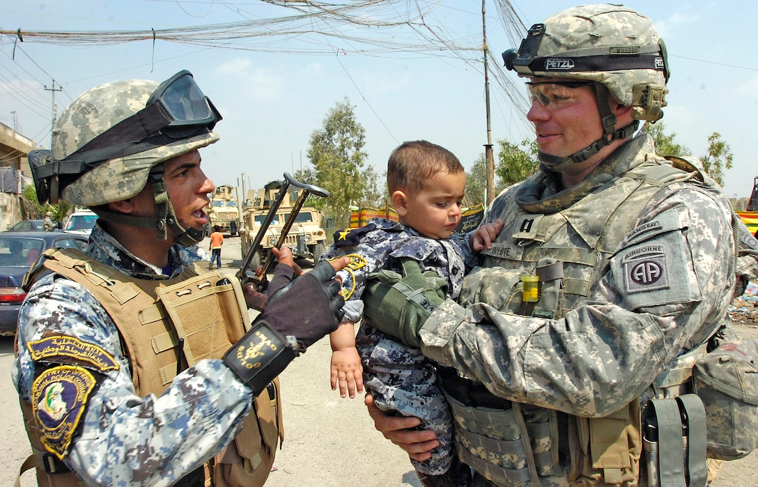 U.S. Army Capt. Clay White, right, talks to an Iraqi police officer as he carries an Iraqi child wearing a police uniform following a school supply distribution in eastern Baghdad, Iraq, April 1, 2009. White, a company commander, is assigned to the 82nd Airborne Division's Company C, 2nd Battalion, 505th Parachute Infantry Regiment, 3rd Brigade Combat Team. U.S. Iraqi officials invited U.S. paratroopers to participate in National Orphan Day across Iraq and more than 60 orphan children received needed goods.