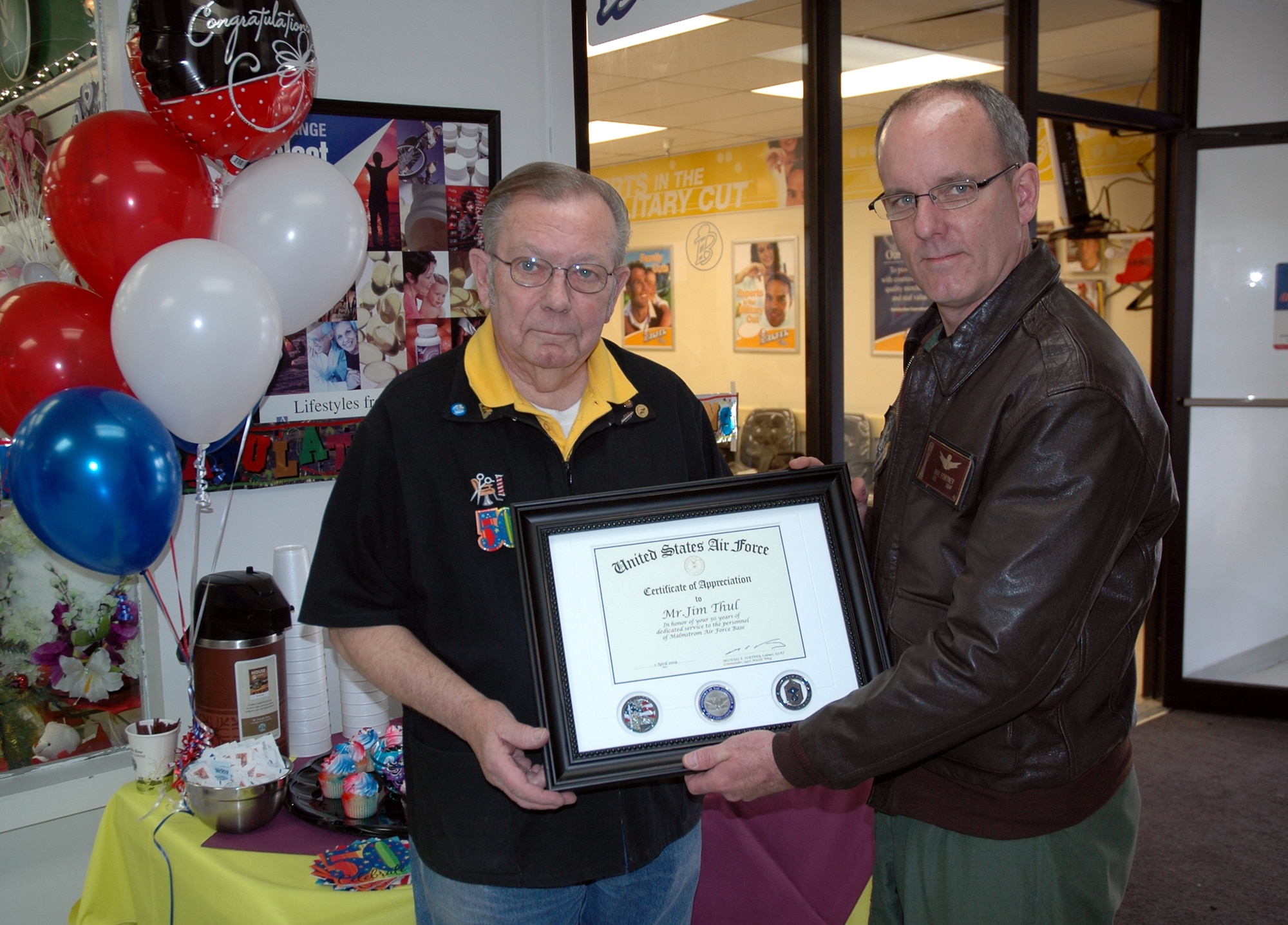 Jim Thul and Col. Mike Fortney, 341st Missile Wing commander,  pose for a photo while they hold a certificate of appreciation presented to Mr. Thul in recognition of his 50 years of service to Malmstrom Air Force Base as a barber and a wing man. Mr. Thul began cutting hair at Malmstrom April 1, 1959. (U.S. Air Force photo/Senior Airman Dillon White)