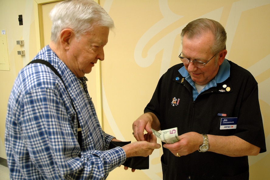 Father Francis McInnis, Malmstrom's contract Catholic priest, pays Jim Thul for a hair cut March 31 at the base barber shop. April 1 marked Mr. Thul's 50th anniversary as a barber at Malmstrom. He has cut Father McInnis's hair since 1970. (U.S. Air Force photo/Senior Airman Dillon White)