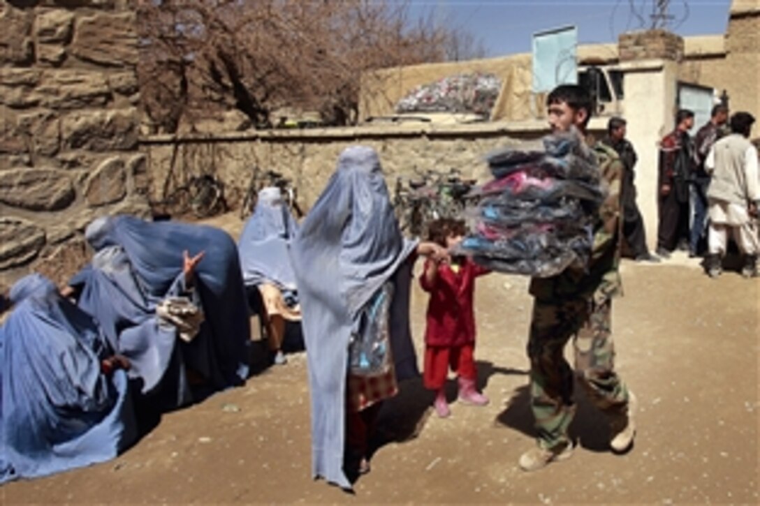 An Afghan National Army commando hands out school bags to women and children during a humanitarian assistance mission at a school in Kabul, Afghanistan, March 25, 2009.