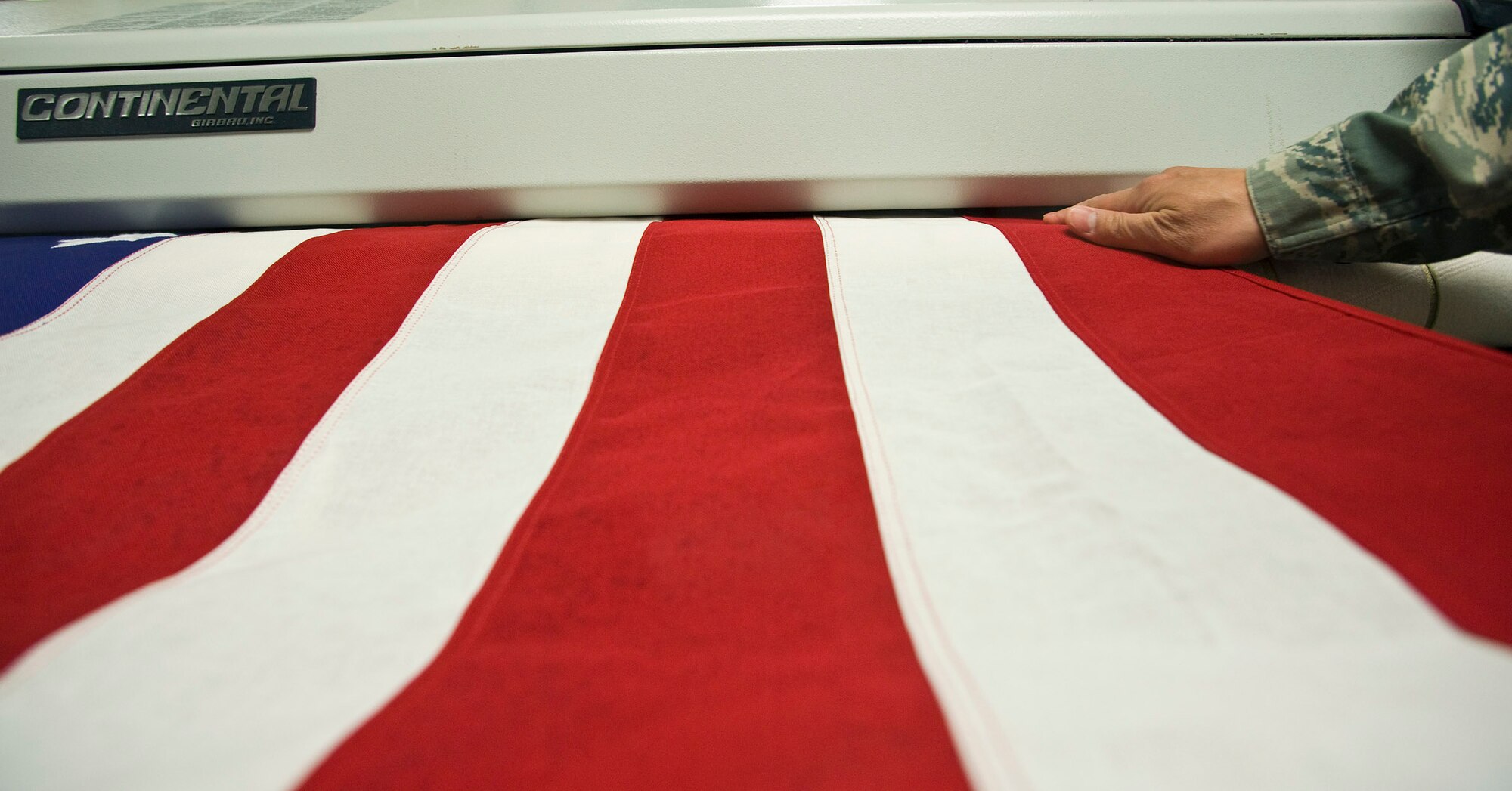 Tech. Sgt. Willard Rico feeds a U.S. flag into a pressing machine March 31 at the Charles C. Carson Center for Mortuary Affairs, Dover Air Force Base, Del.  The press irons the flags wrinkle free that will be placed over caskets during the dignified transfer of remains.  The center is the Defense Department's largest joint-service mortuary facility, and the only one in the continental United States. Sergeant Rico is deployed from the 60th Force Support Squadron, Travis AFB, Calif.  (U.S. Air Force photo/Staff Sgt. Bennie J. Davis III)