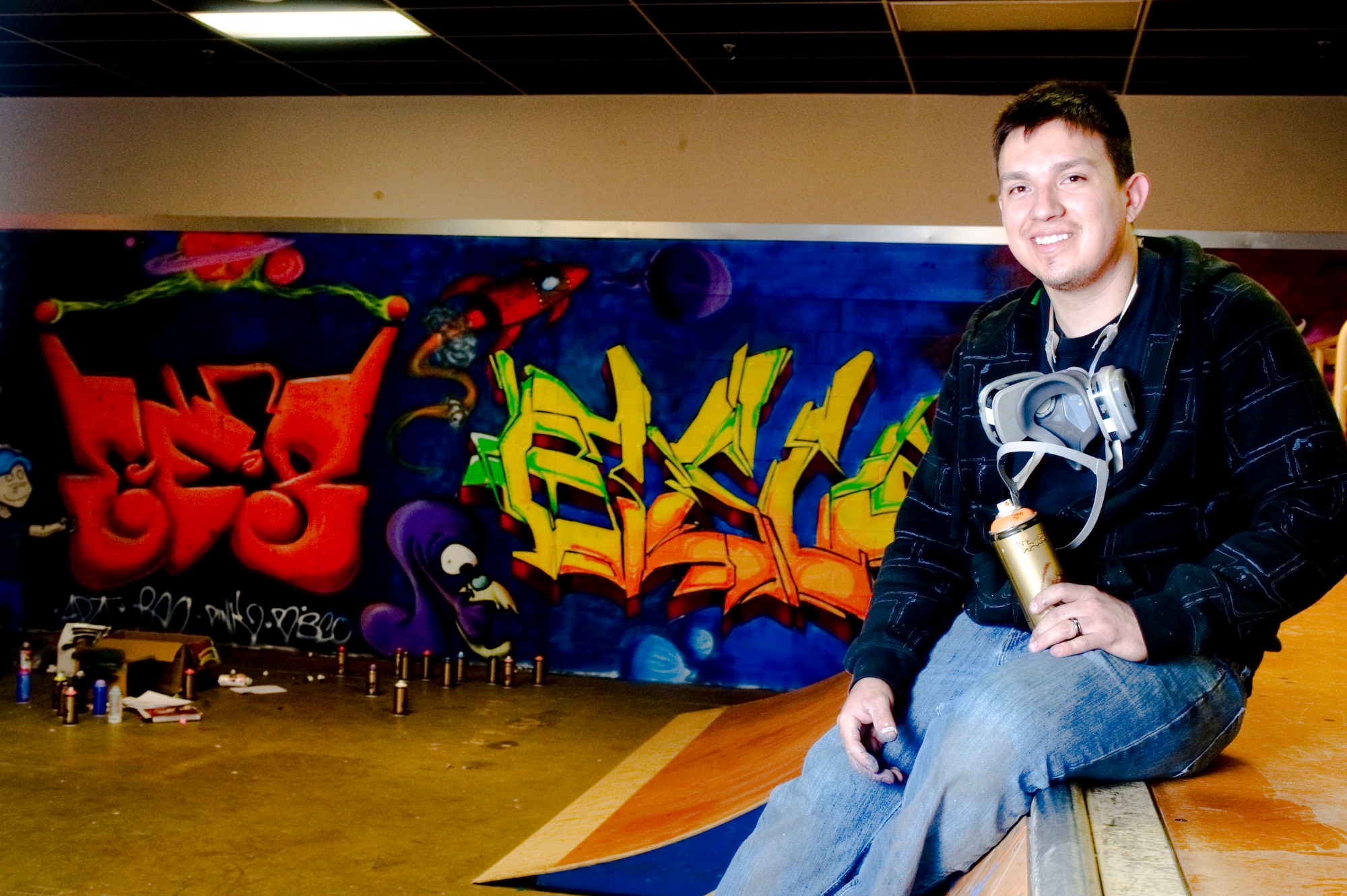 ELMENDORF AIR FORCE BASE, Alaska -- Staff Sgt. Art Delafuente takes a break in front of his graffiti moral at the indoor skate park in the Arctic Oasis Community Center April 3, 2009. Delafuente is a crew chief from 19th Aircraft Maintenance Unit and has spent countless hours volunteering to paint the skate park with graffiti. (U.S. Air Force photo by Senior Airman Jonathan Steffen) 
