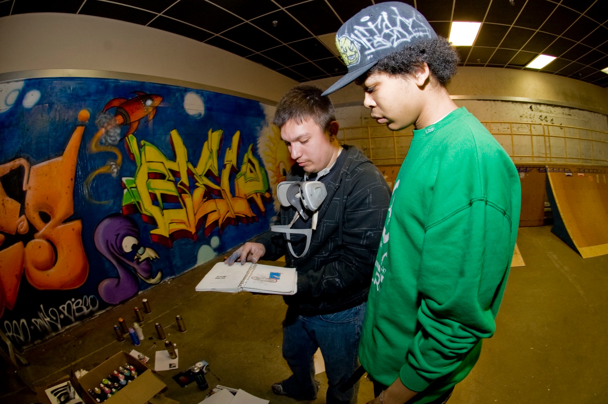 ELMENDORF AIR FORCE BASE, Alaska -- Staff Sgt. Art Delafuente and Arielo Taylor, a civilain, collaborate on a graffiti design to paint at the indoor skate park inside of Arctic Oasis Community Center April 3, 2009. Delafuente is a crew chief from 19th Aircraft Maintenance Unit and has spent around 50 hours volunteering to decorate the skate park with graffiti. (U.S. Air Force photo by Senior Airman Jonathan Steffen) 