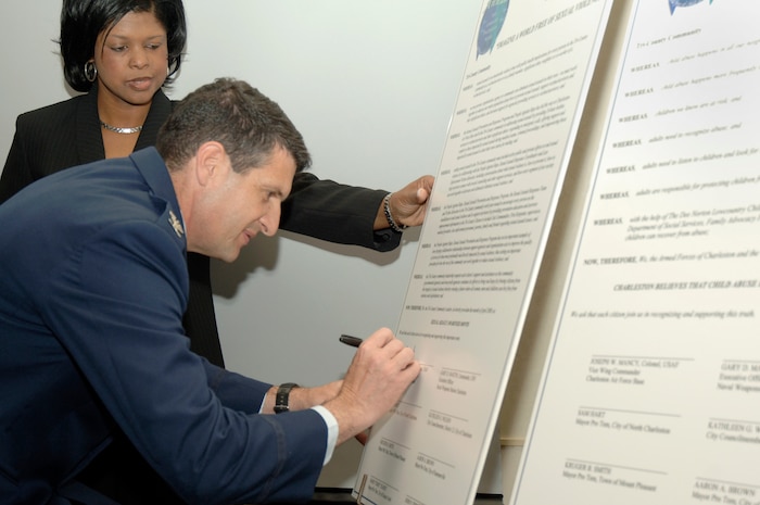 Veronica Griffin watches as Col Joseph Mancy signs a proclamation during the 2nd Annual Joint Community Proclamation Signing ceremony at the Charleston Club April 2. The signing of the proclamation continues collaboration with local communities and military installations for prevention of sexual assault and child abuse. Representatives from six nearby communities, along with the Naval Weapons Station Charleston, joined Charleston AFB in signing the proclamation. Ms. Griffin is the installation sexual assault response coordinator and Colonel Mancy is the acting 437th Airlift Wing vice commander.  (U.S. Air Force photo/Staff Sgt. Marie Cassetty)
