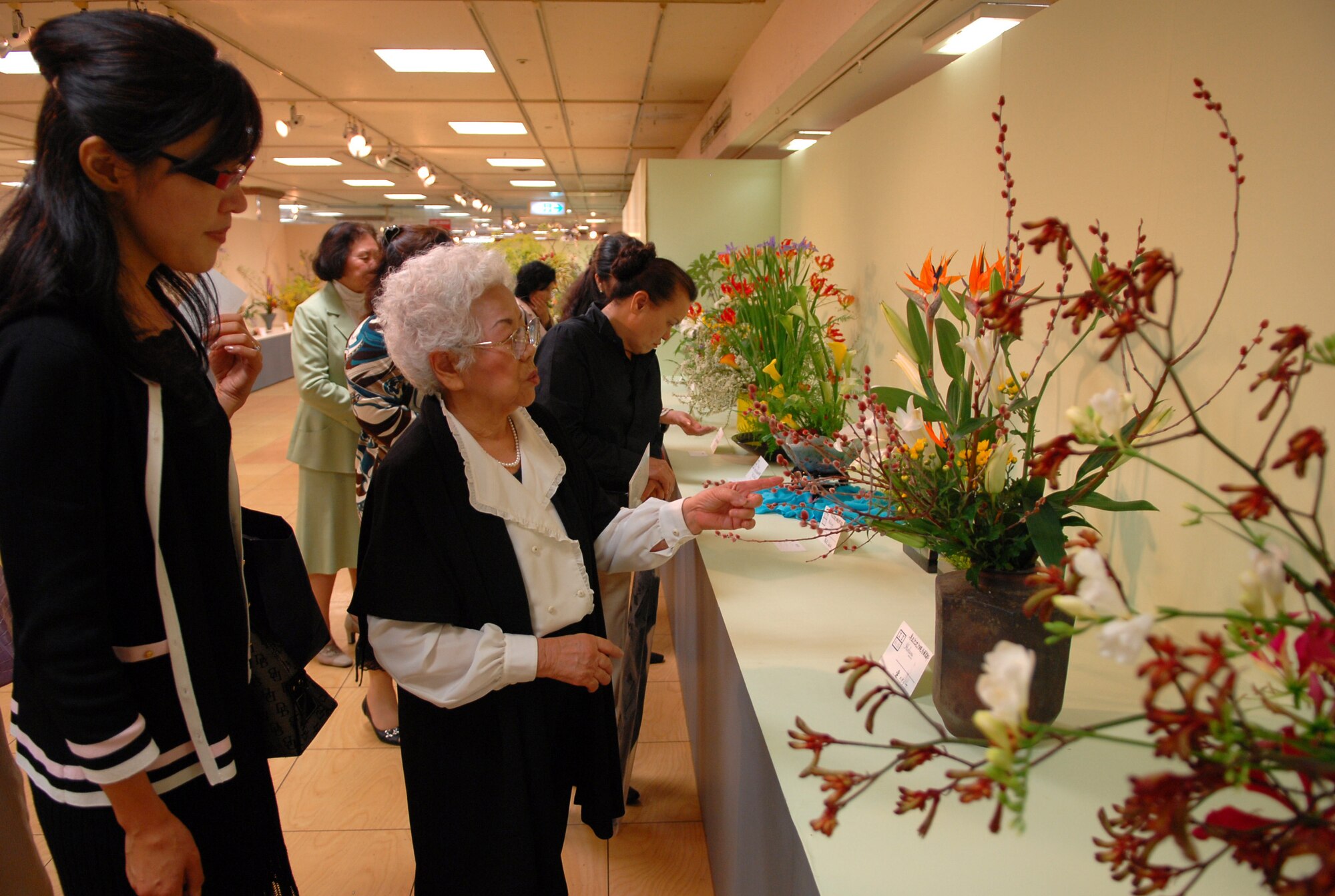 Keiko Nakajima Robbins (far right), founding member of Okinawaís Ikebana International since 1956 and Ikebana teacher at the Kadena Air Base USO, talks with her student Ryoko Vogel (far left), wife of a Navy civilian working at Kadena Air Base, about her work displayed far right.  Ms. Vogel is also the third vice president of Ikebana International Okinawa Chapter and studies ikebana at the Kadena USO. In October, the Ikebana International Okinawa Chapter and some students from the Kadena USO will go to the White House in Washington, D.C., for a flower demonstration and lecture. (U.S Air Force photo/Junko Kinjo)  