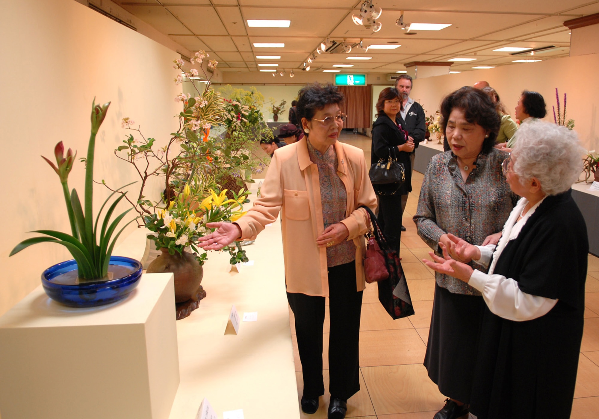 Keiko Nakajima Robbins (far right), founding member of Okinawaís Ikebana International since 1956 and Ikebana teacher at the Kadena Air Base USO, talks about her ikebana flower arrangement to far left of the visitors at the 51st Ikebana International Okinawa Chapter 10 Charity Flower Exhibition.  The event was held March 27-29 at the Okinawa Mitsukoshi Department Store in Naha, Okinawa. In October, the Ikebana International Okinawa Chapter and some students from the Kadena USO will go to the White House in Washington, D.C., for a flower demonstration and lecture. (U.S Air Force photo/Junko Kinjo)