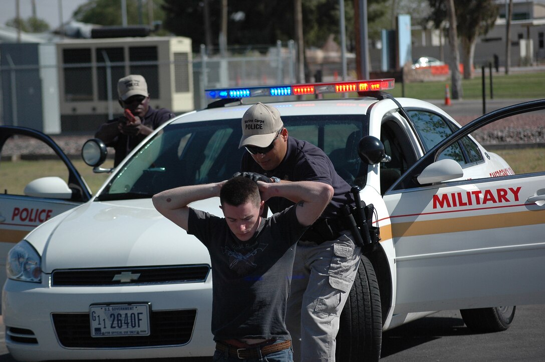 Jose Arguelles, Marine Corps Air Station Yuma, Ariz., Marine Corps Police Academy cadet, searches Pfc. Paul Henry while Jazz Sadik, academy cadet, provides cover during a known-risk traffic stop exercise in a parking lot on station April 8, 2009. Arguelles and Sadik are part of the last class of cadets to be trained by the Yuma academy. Future station cadets will be sent to the Marine Corps Air Station Miramar, Calif., academy, along with cadets from other West Coast installations.