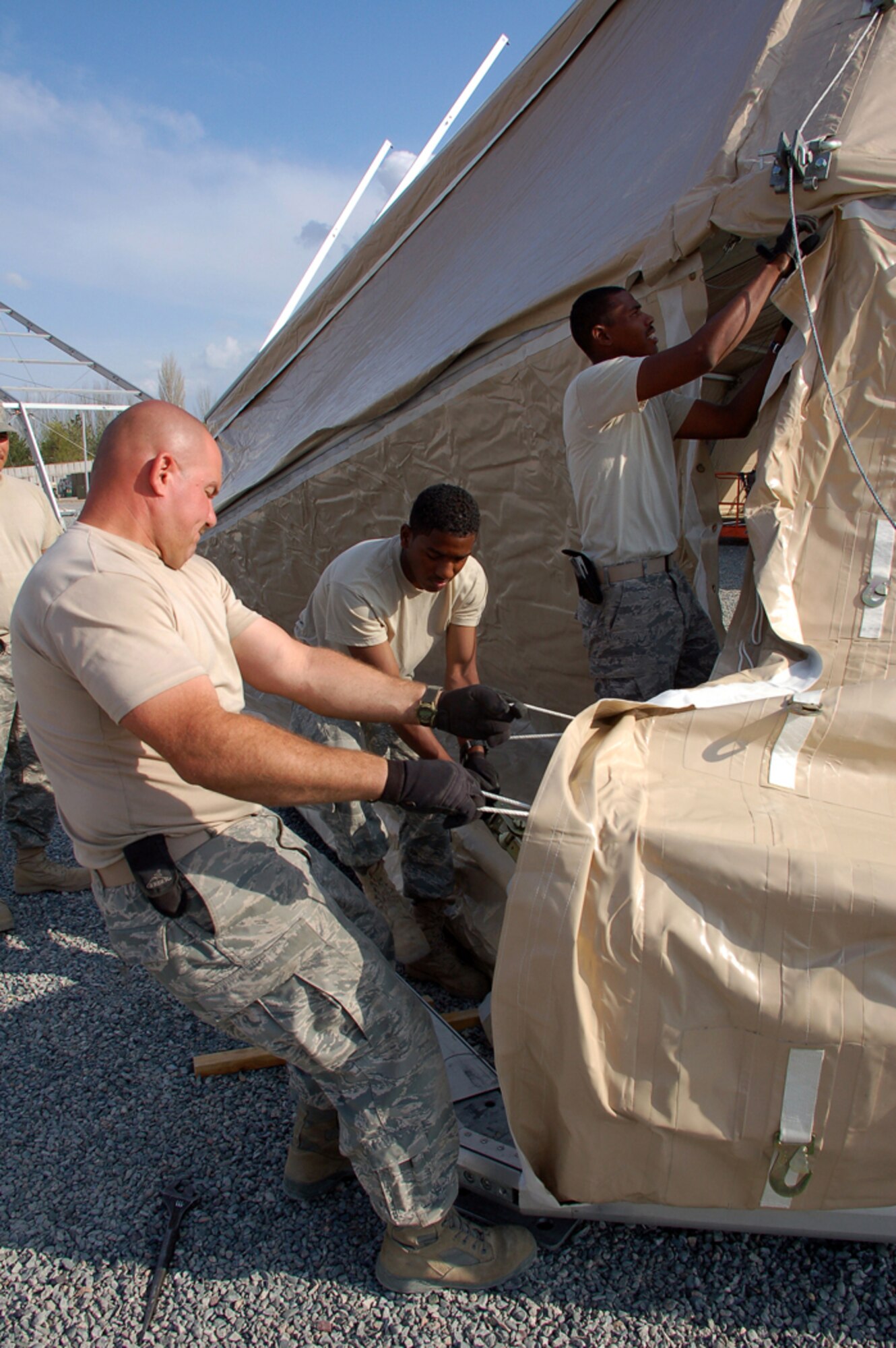 Master Sgt. Ryan Yeggy and Senior Airman Alii Chun pull together the front flaps of a 4,000 square-foot dome shelter while Staff Sgt. Timothy Robinson laces the panels together during a construction project April 1 at Manas Air Base, Kyrgyzstan. Two of the structures are being erected in preparation for the increased number of coalition personnel transiting through Manas to and from Afghanistan. The Airmen are assigned to a nine-person Basic Expeditionary Airfield Resources team deployed to Southwest Asia. All of the team members are deployed from Holloman Air Force Base, N.M. (U.S. Air Force photo/Tech. Sgt. Phyllis Hanson) 
