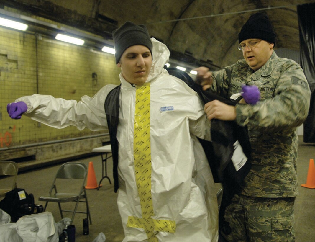 Tech. Sgt. Michael Foster aides Airman 1st Class Samuel Mericle, members of the Air Force District of Washington CBRNE response force, with putting on his utility vest before responding to a chemical attack during the training scenario at the Center for National Response in Gallagher, W. Va. April 1. The utility vest is used to hold a powered air purifying respirator that filters air that might contain toxic fumes. (U.S. Air Force photo/ Senior Airman Renae Kleckner)