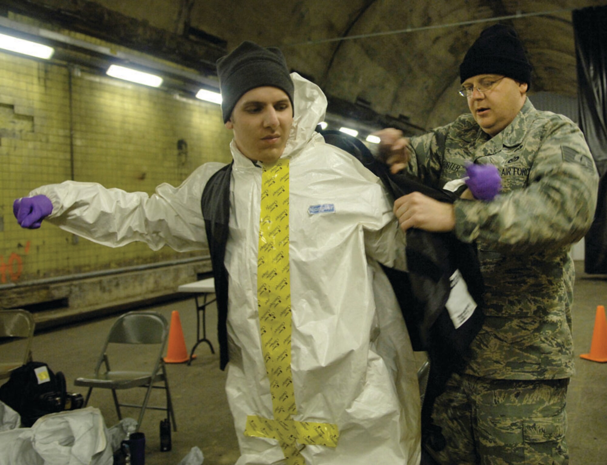 Tech. Sgt. Michael Foster aides Airman 1st Class Samuel Mericle, members of the Air Force District of Washington CBRNE response force, with putting on his utility vest before responding to a chemical attack during the training scenario at the Center for National Response in Gallagher, W. Va. April 1. The utility vest is used to hold a powered air purifying respirator that filters air that might contain toxic fumes. (U.S. Air Force photo/ Senior Airman Renae Kleckner)