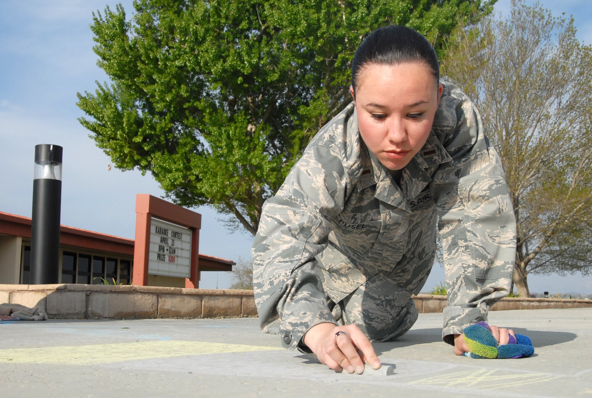 Second Lt. Julia Pusel, 95th Communications Squadron unit project manager, draws a chalk advertisement for Earth Day in front of the Oasis Community Center April 14. This is part of Edwards' Earth Day celebration April 21 at the Center of Excellence. The basewide event is hosted by Environment Management, with the theme "Living a Sustainable Life." (U.S. Air Force photo/Senior Airman Julius Delos Reyes)
