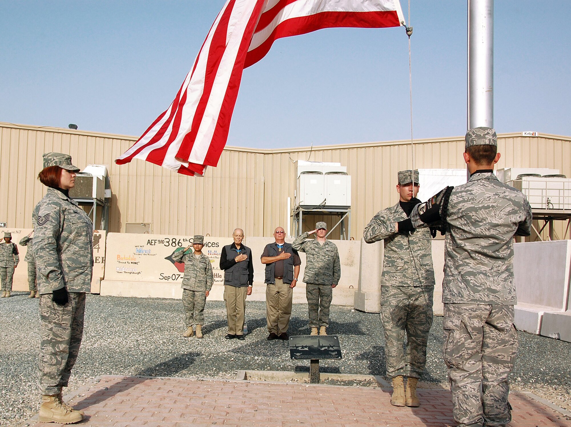 Medal of Honor recipients retired Army Col. Robert Howard and retired Army Command Sgt. Maj. Gary Littrell watch as members of the 386th Air Expeditionary Wing honor guard conduct a retreat ceremony April 10 at an air base in Southwest Asia. Colonel Howard and Sergeant Major Littrell visited with members of the 386th AEW during a Medal of Honor Society tour of the U.S. Air Forces Central area of responsibility, speaking to Airmen on the importance of what they do and thanking them for their service. (U.S. Air Force photo illustration) 
