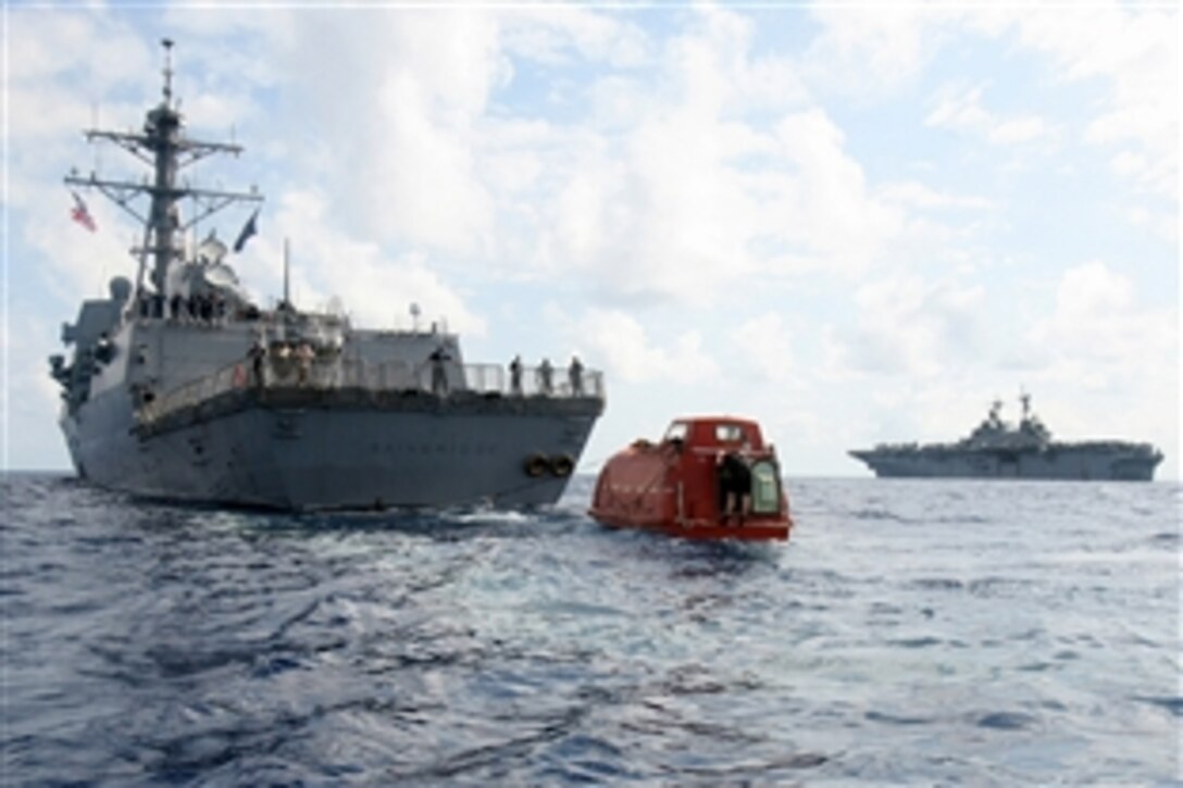 The guided-missile destroyer USS Bainbridge tows the lifeboat from the Maersk-Alabama to the amphibious assault ship USS Boxer, in background, April 13, 2009, to be processed for evidence after the successful rescue of Capt. Richard Phillips. Phillips was held captive by suspected Somali pirates in the lifeboat in the Indian Ocean for five days after a failed hijacking attempt off the Somali coast. 