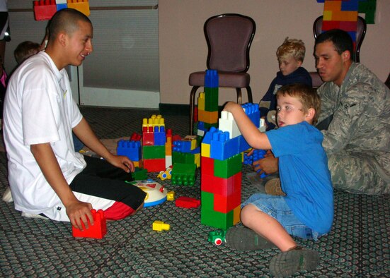 (Left) Airman 1st Class Bryant Yanez, 325th Security Forces Squadron member, and Airman Christopher Allen, 325th Force Support Squadron Flight Kitchen cook, build lego towers with childen of deployed members during the Tyndall Airman and Family Readiness Center "Hearts Apart Spa Night." While the childrens' parents enjoyed the spa activities, more than 40 volunteers provided free child care, overseeing and playing with the kids. Along with the play area, children also took part in arts and crafts, as well as watching movies. (U.S. Air Force photo/SSgt Joshua Stevens)