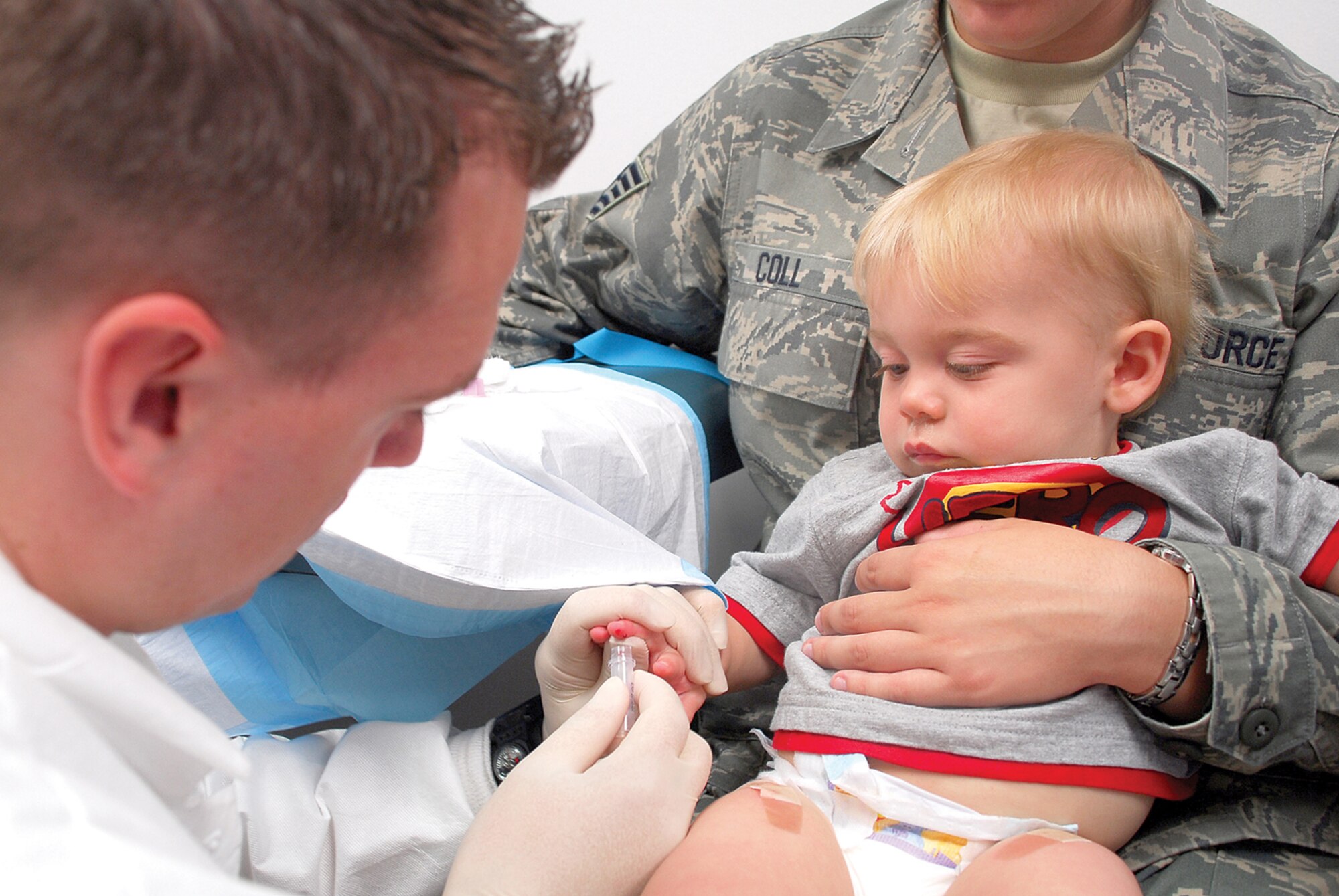Senior Airman Troy Fred, 56th Medical Support Squadron medical laboratory technician, extracts blood from the finger of Alexander Coll, 1, to perform a complete blood count. (U.S. Air Force photo/ Airman 1st Class Traci Forte.)