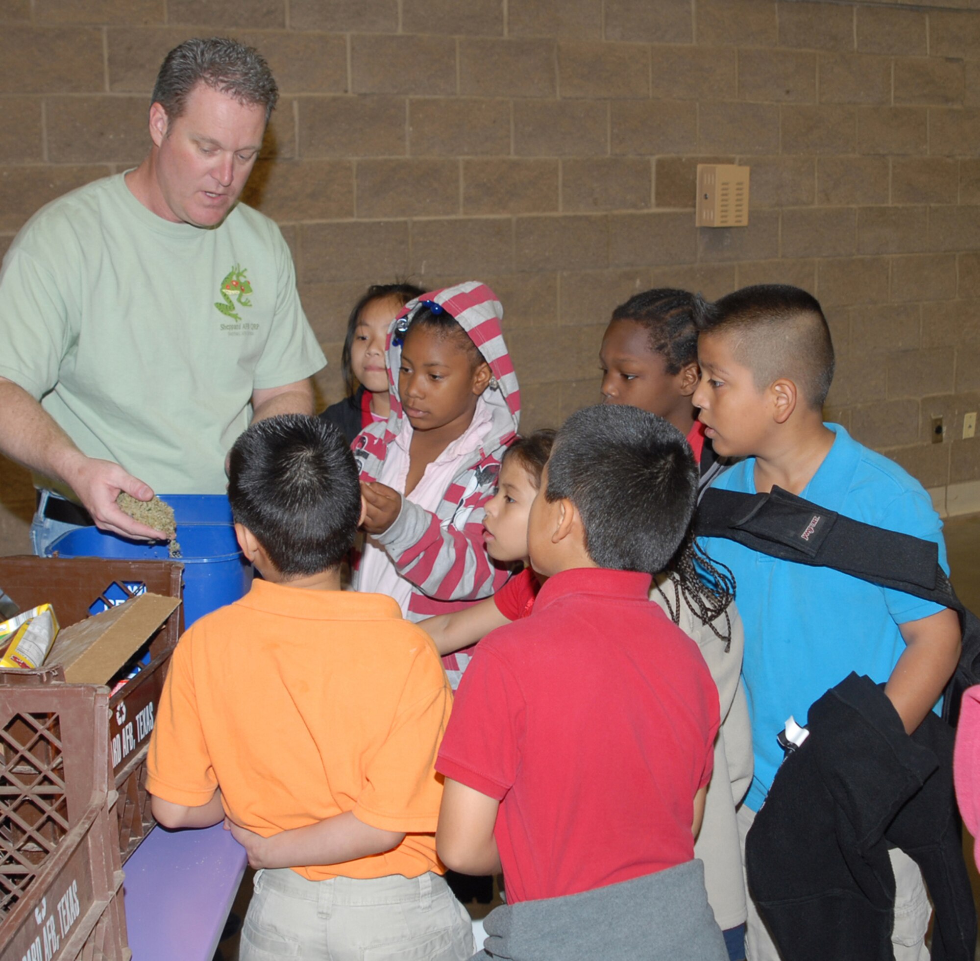 Rick Milhollon, the 82nd Civil Engineering Squadron Environmental Flight chief,  hands out pencils, made from recycled rubber tires, while educating students that paper, cans, cardboard, bottles, plastic and computer cartridges items are all recyclable. Excited oohs and aahs rose as hesitant hands delved in to buckets of recycled bottles crushed into various stages of sand.  The crushed bottles are then used for yard and road filler or decorative landscape material. (U.S. Air Force photo/Lou Anne Sledge)