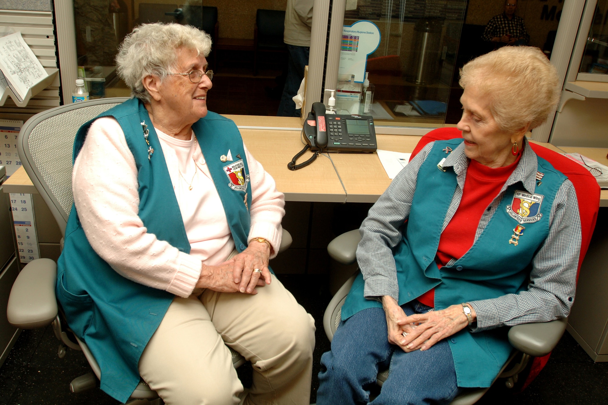 Gary Johnson (left), and Anita Gibba, clinic entrance information desk volunteers, discuss their years at the hospital on April 8, at Wilford Hall Medical Center, Lackland Air Force Base, Texas.  Gary has been volunteering at Wilford Hall for 28 years and Anita for 7 years.  Volunteer appreciation week begins April 19 thru April 25.  (U.S. Air Force photo by Senior Airman Nicole Roberts)