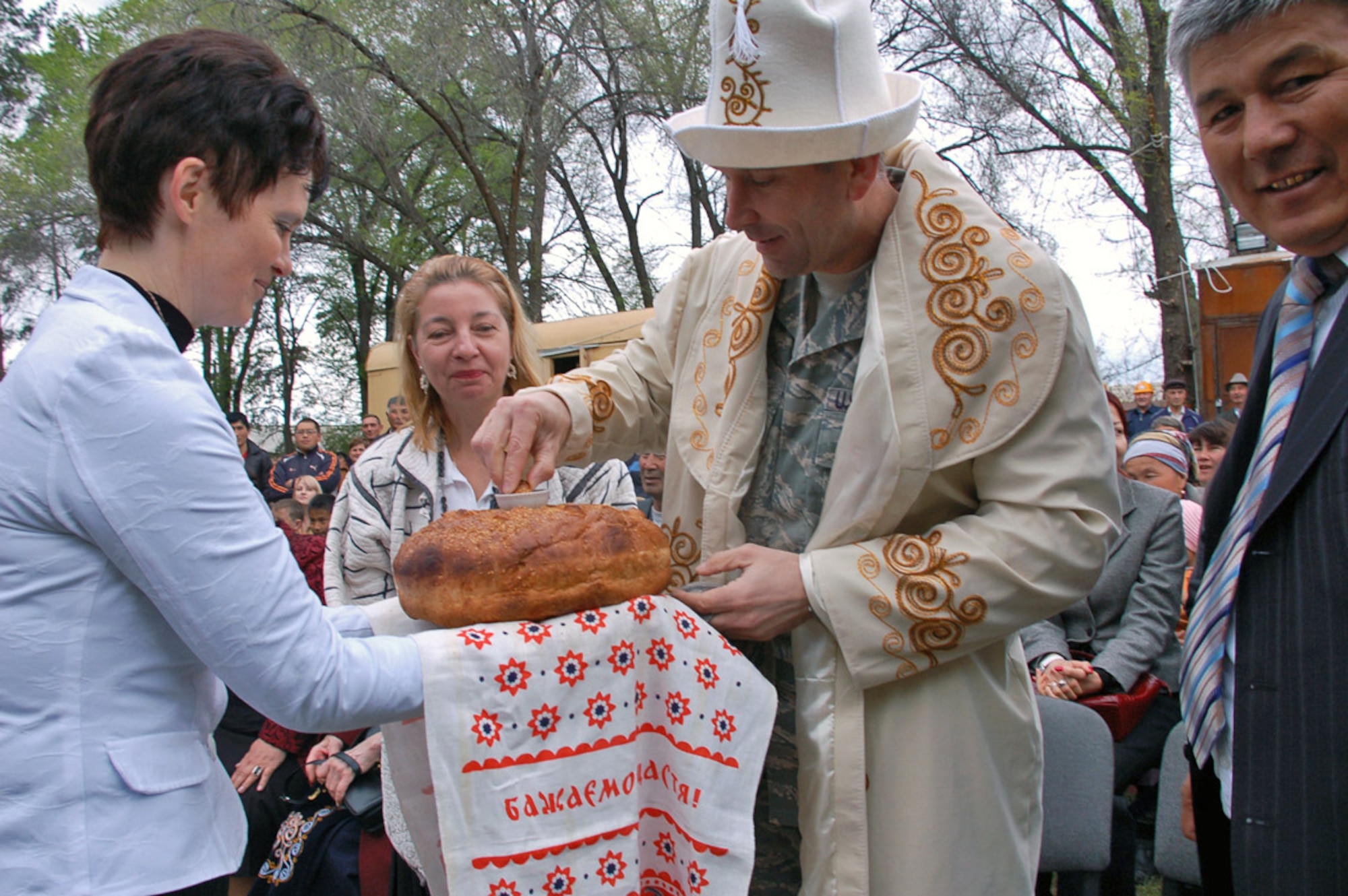 During the Birdik Village School ground-breaking ceremony April 14, Principal Olga Voroshihina (left) shares homemade bread, called nan, with Manas Air Base commander Col. Christopher Bence. The U.S. Ambassador to Kyrgyzstan Tatiana Gfoeller and Birdik Village Mayor Syrgak Kydykeev also broke bread to symbolize peace, prosperity and good progress for the $470,000 project. The colonel is wearing a ceremonial robe called a chapan and a traditional felt hat called a kalpak. (U.S. Air Force photo/Tech. Sgt. Phyllis Hanson)