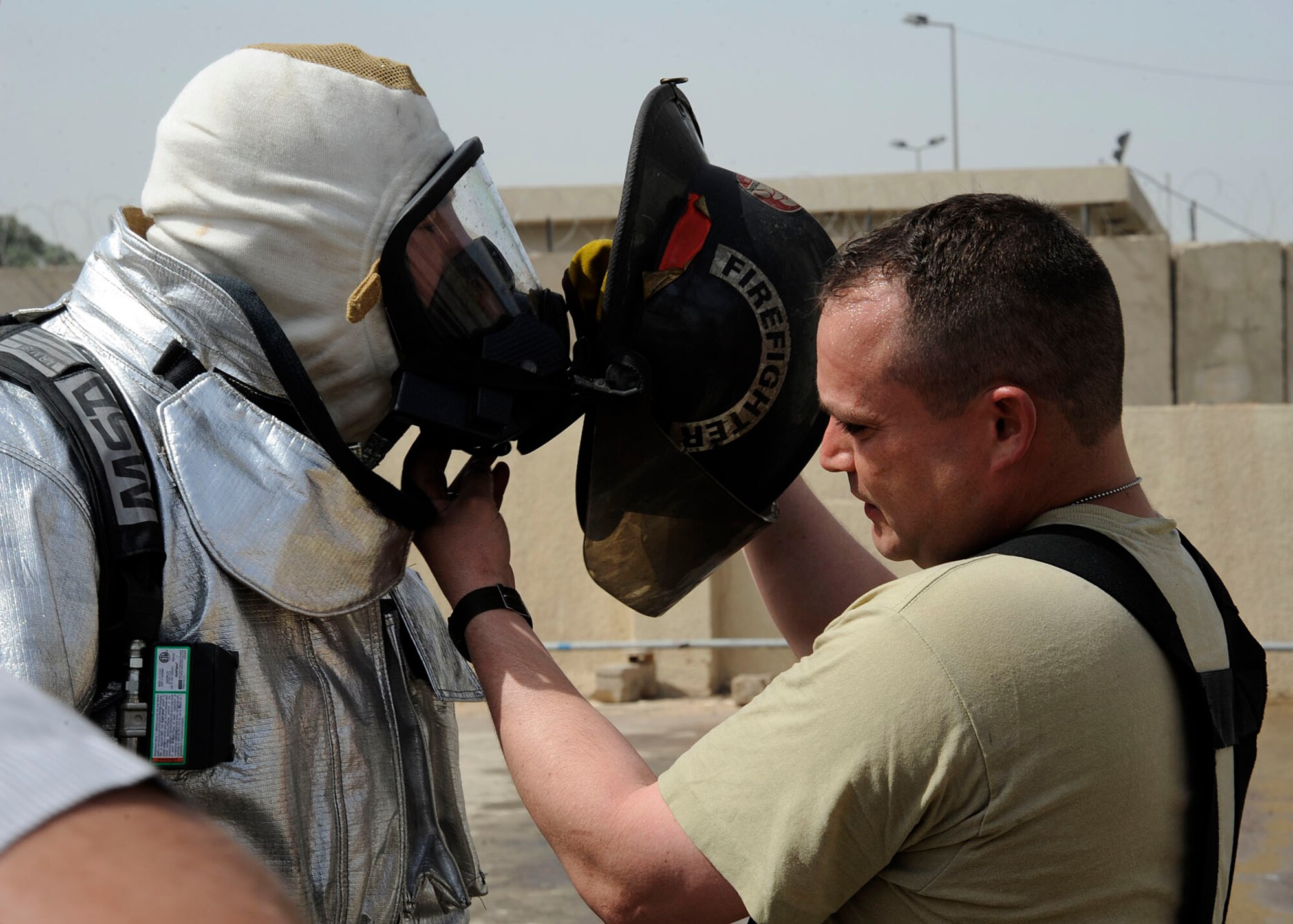Tech. Sgt. Brian Partido, 821st Basic Technical Training Squadron, Coalition Air Force Transition Team fire rescue advisor, helps fellow instructor and advisor, Tech. Sgt. Jay Wingfield, with his helmet before a live fire exercise in Baghdad, Iraq April 13, 2009.  Sergeants Partido and Wingfield train students of the Iraqi Joint Fire Academy in the practical portion of the course.  The two-month course is made up of 26 students from the Iraqi air force and Iraqi civil defense.  Sergeant Partido is deployed from the 19th Civil Engineer Squadron in Little Rock Air Force Base, Ark., and is a native of El Paso, Texas.  Sergeant Wingfield is deployed from Goodfellow AFB, Texas and is a native of Peoria, Ill.  (U.S. Air Force photo by Senior Airman Jacqueline Romero)