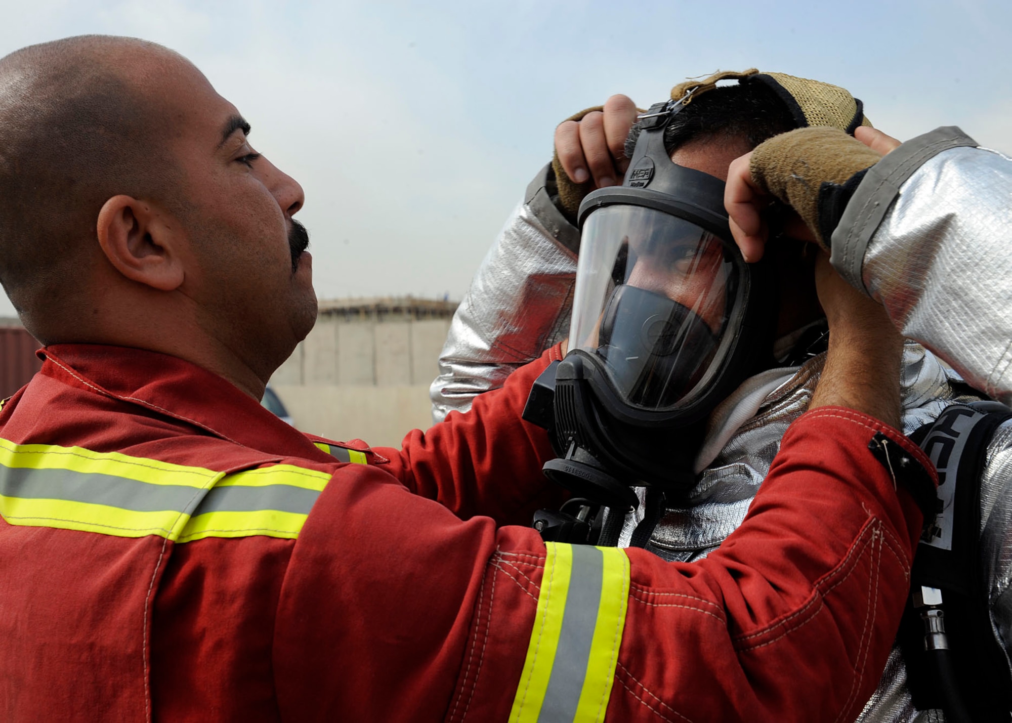 Members of the Iraqi air force and Iraqi civil defense works as a team ensuring their masks are secure. .  The servicemembers are going through the Basic Fire Course at the Iraqi Joint Fire Academy in Baghdad, Iraq April 11, 2009. The trainees prepare to experience a live car burn training exercise, which will ensure they can translate what was learned in the classroom to real live scenarios. This class of 26 students is the largest the academy has pushed through for the two month course.  (U.S. Air Force photo by Senior Airman Jacqueline Romero)
