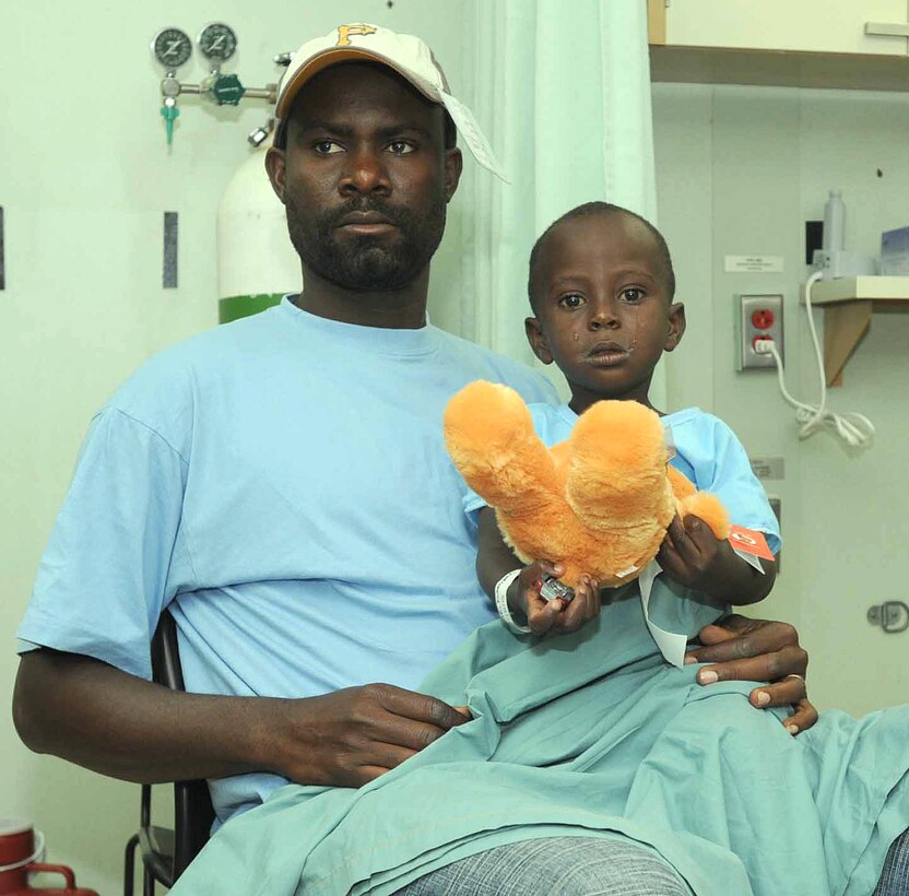A Haitian boy holds on to his teddy bear with his father while waiting for surgery  on board the military hospital ship USNS Comfort in Port au Prince, Haiti, April 14, 2009.