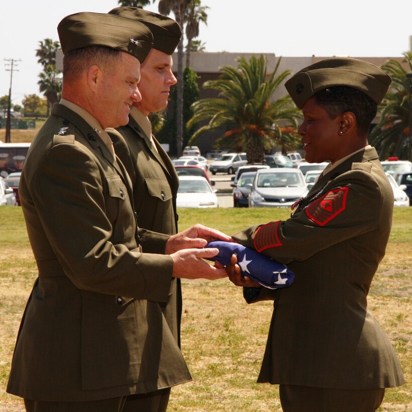 Major Gen. Michael R. Lehnert, commanding officer, Marine Corps Installations West, stands alongside his new sergeant major, Sgt. Maj. Jeffery H. Dixon, as he hands his former advisor, Sgt. Maj. Barbara J. Titus a flag flown above the national capitol building for her retirement.