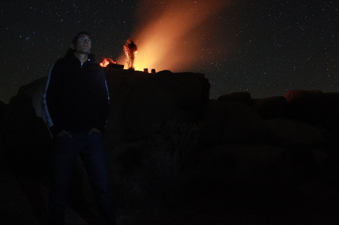 Lance Cpl. Aaron Kristopik, a paralegal clerk with the Combat Center’s Staff Judge Advocate and a native of New Britain, Conn., soaks–in the night sky April 18 night in the Mojave National Preserve as his friends cook over the fire in the background.