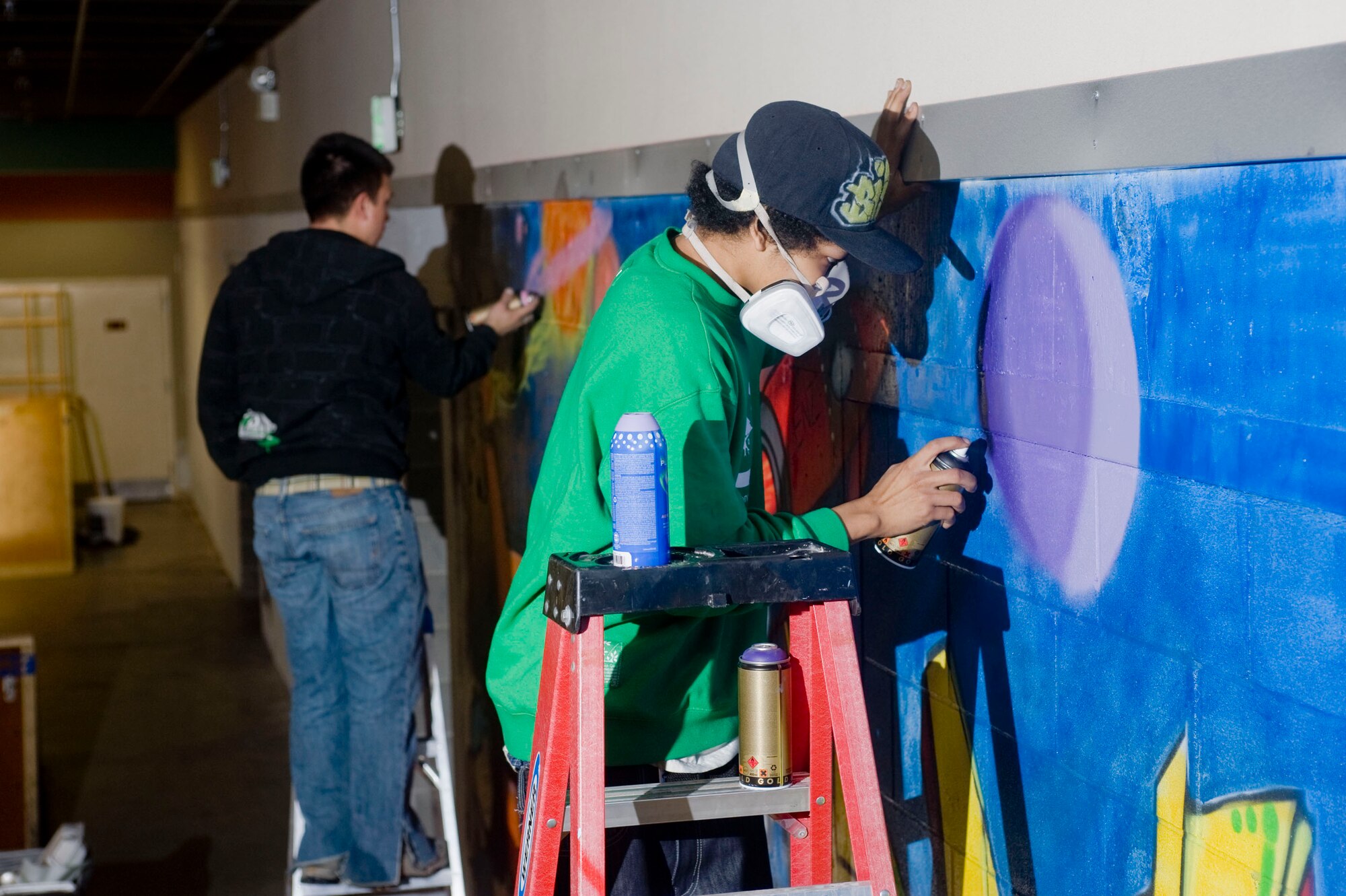 Staff Sgt. Art Delafuente and Arielo Taylor paint a wall at the indoor skate park inside the base community center April 3 at Elmendorf Air Force Base, Alaska. Sergeant Delafuente is a crew chief from 19th Aircraft Maintenance Unit. He and Mr. Taylor volunteered to decorate the skate park with graffiti. (U.S. Air Force photo/Senior Airman Jonathan Steffen)