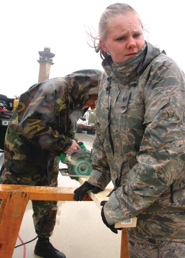 Staff Sgt. Amanda Fischer, 316 CES construction journeyman, holds a two-by-four steady as Tech. Sgt. Miguel Lopez uses a circular saw to cut wood for the make-shift frame Wednesday. (U.S. Air Force photo/ Bobby Jones)