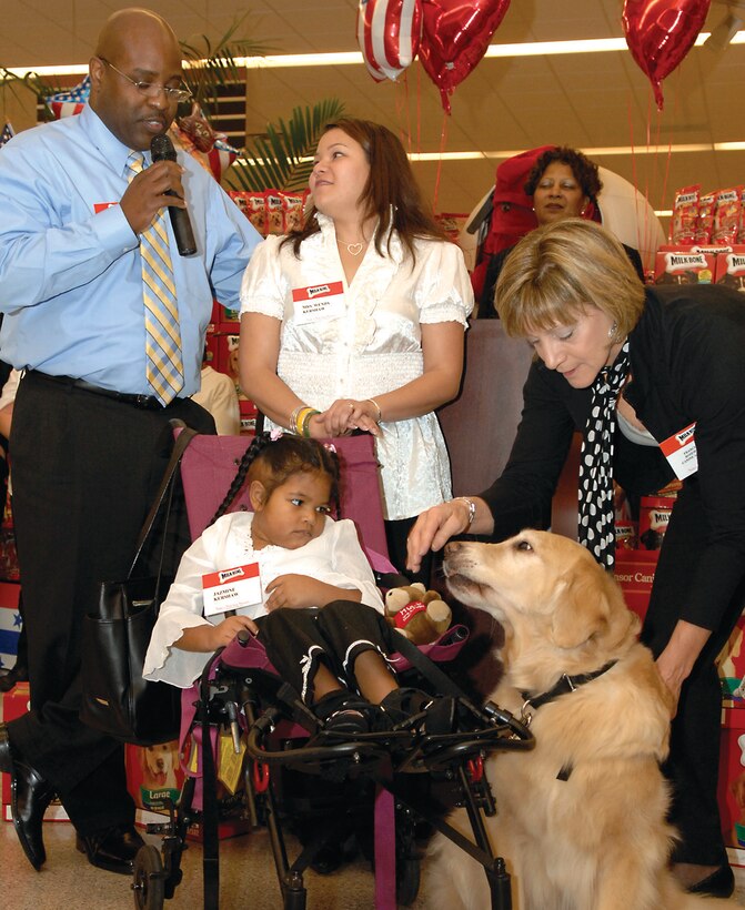Jazmine Kershaw, 9, bottom center, daughter of Master Sgt. (ret.) Michael Kershaw, left, and his wife Wendy Kershaw, center, receives a new canine as part of  the Canine Heroes Program at the Commissary Wednesday. Jazmine’s father gives thanks as his daughter is presented the canine  by a representative. Through the Canine Heroes Progam, functionally impared children are offered trained dogs as assistants. The dogs are taught to obey voice commands and assist their owner with many tasks such as turning on the lights, opening doors and helping with the laundry. (U.S. Air Force photo/ Senior Airman Giang Nguyen)