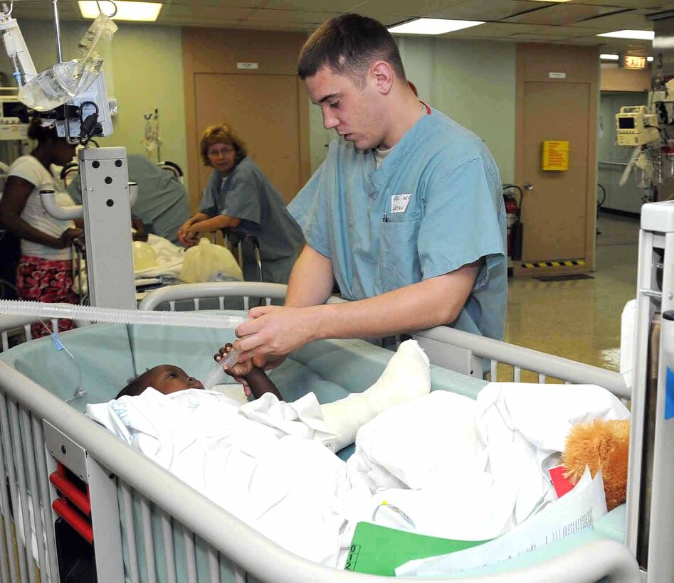 U.S. Navy Spc. Timothy Warren, assigned to the 807th Medical Command, holds the hand of a Haitian girl in the post-anesthesia care unit aboard the military hospital ship USNS Comfort in Port au Prince, April 16, 2009. Comfort is part Continuing Promise 2009, a four-month humanitarian and civic assistance mission to Latin America and Caribbean.