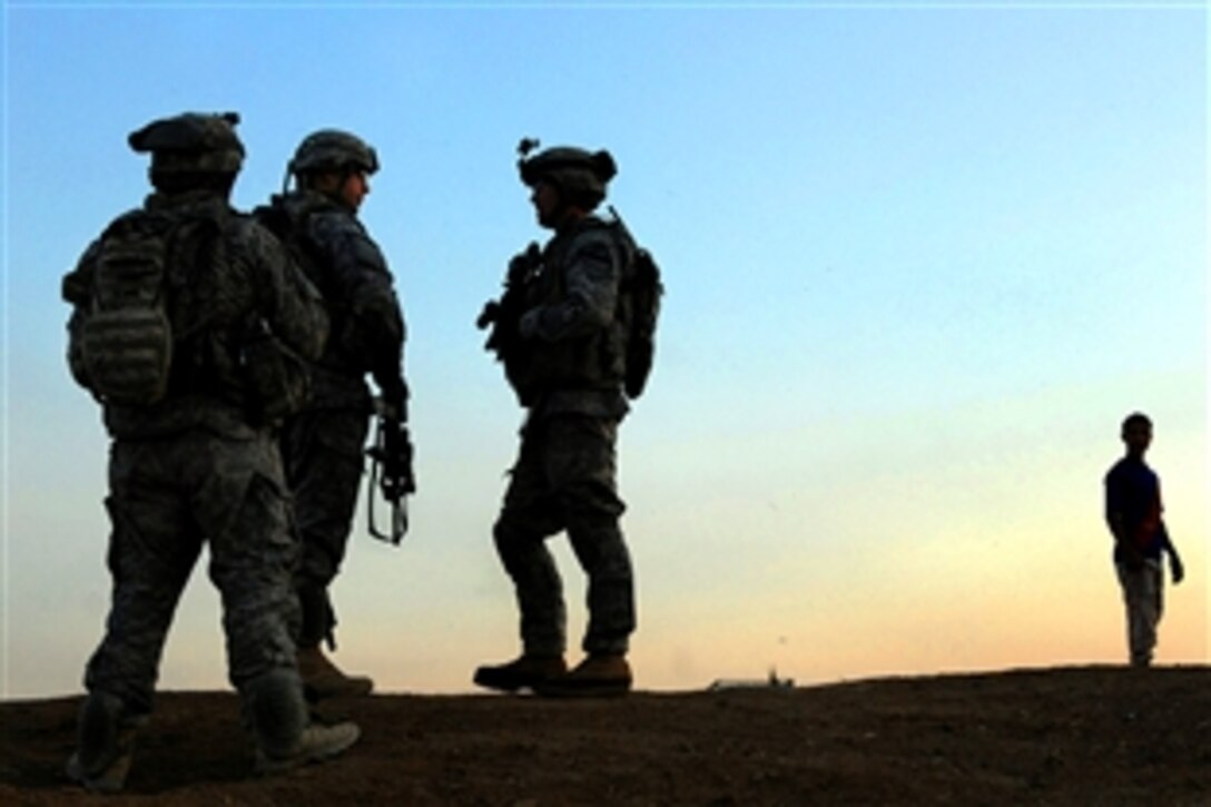 U.S. Army soldiers stand guard while an Iraqi man watches in the distance as the sun sets at the beginning of a patrol during Operation Magnon al-Wombet in Shaab, Iraq, April 10, 2009. The operation was designed to stop the flow of improvised explosive devices, weapons and contraband from the outskirts of the city into its center. The soldiers are assigned to Troop E, 1st Battalion, 5th Cavalry Regiment.