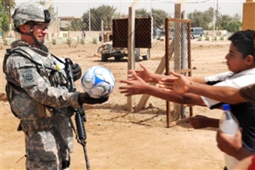 U.S. Army 1st Lt. Benjamin Martin prepares to hand a soccer ball to a charging group of Iraqi children during a site-assessment mission in the Al-Madain area of eastern Baghdad, Iraq, April 18, 2009. Martin, assigned to the 82nd Airborne Division's Company B, 3rd Brigade Combat Team, is the company's executive officer.