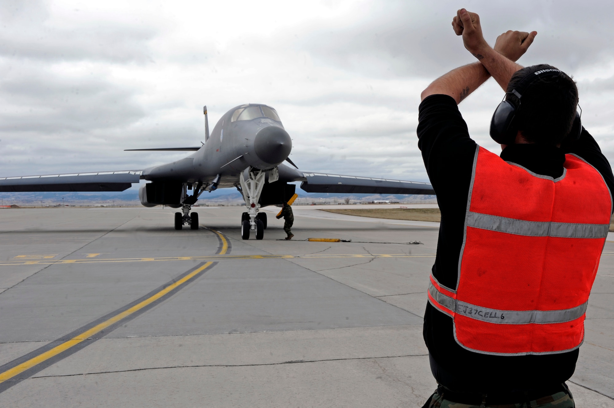 Senior Airman Anthony Blumberg, 28th Aircraft Maintenance squadron crew chief, marshals a B-1B Lancer while Senior Airmen Chris Lee, 28 AMXS crew chief, lays tire chocks at the north end of the flight line here, April 17. The B-1 carries the largest payload of both guided and unguided weapons in the Air Force inventory and is the backbone of America's long-range bomber force. (U.S. Air Force photo/Airman 1st Class Matthew Flynn)