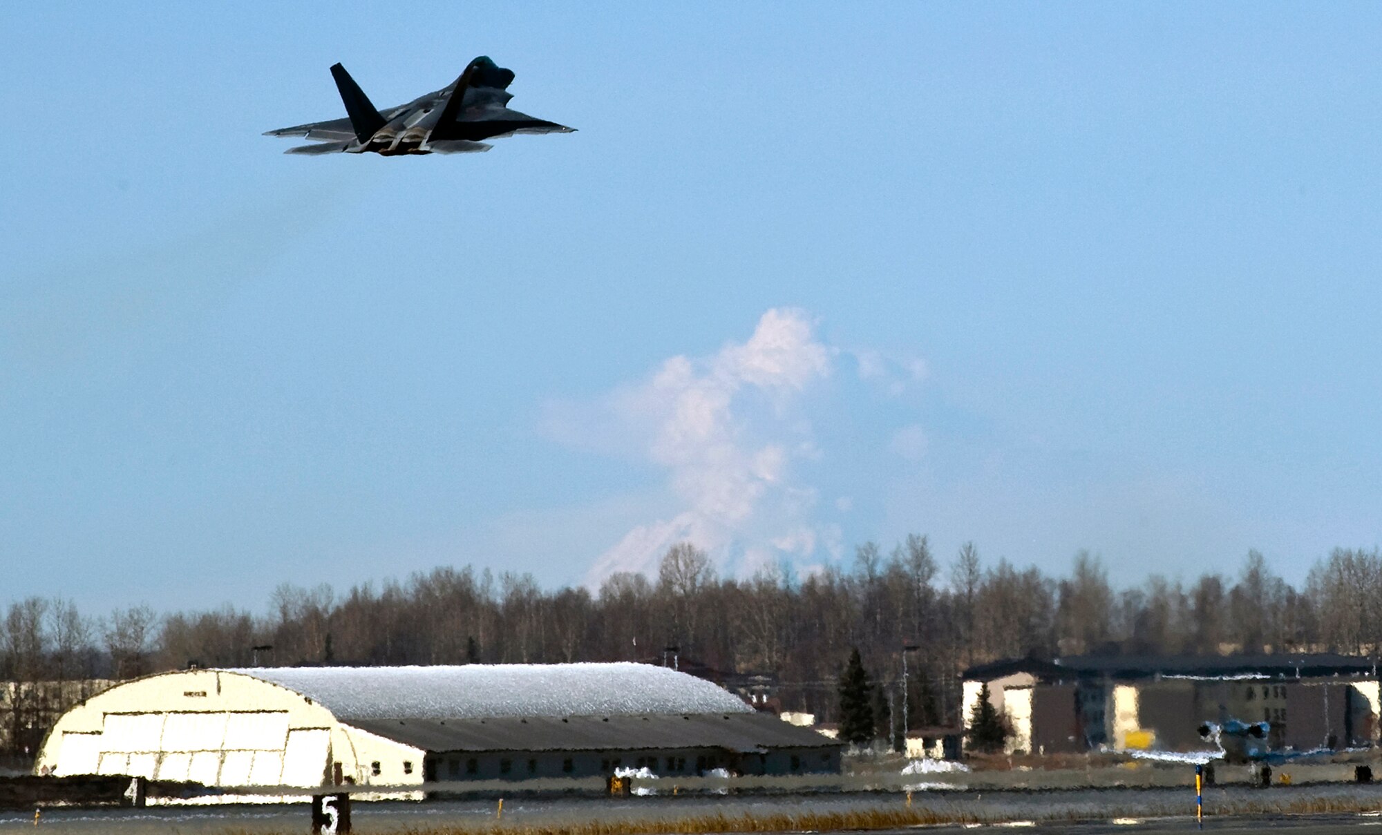 An F-22 Raptor takes off from Elmendorf Air Force Base, Alaska, while Mount Redoubt spews steam into the morning sky. Mount Redoubt, which is 100 miles southwest of Elmendorf, has been active for months, and is keeping emergency managers and early warning personnel on the edge of their seats with periodic eruptions and discharges of steam. So far only a small amount of volcanic ash has fallen on the base. (U.S. Air Force photo/Master Sgt Keith Brown)