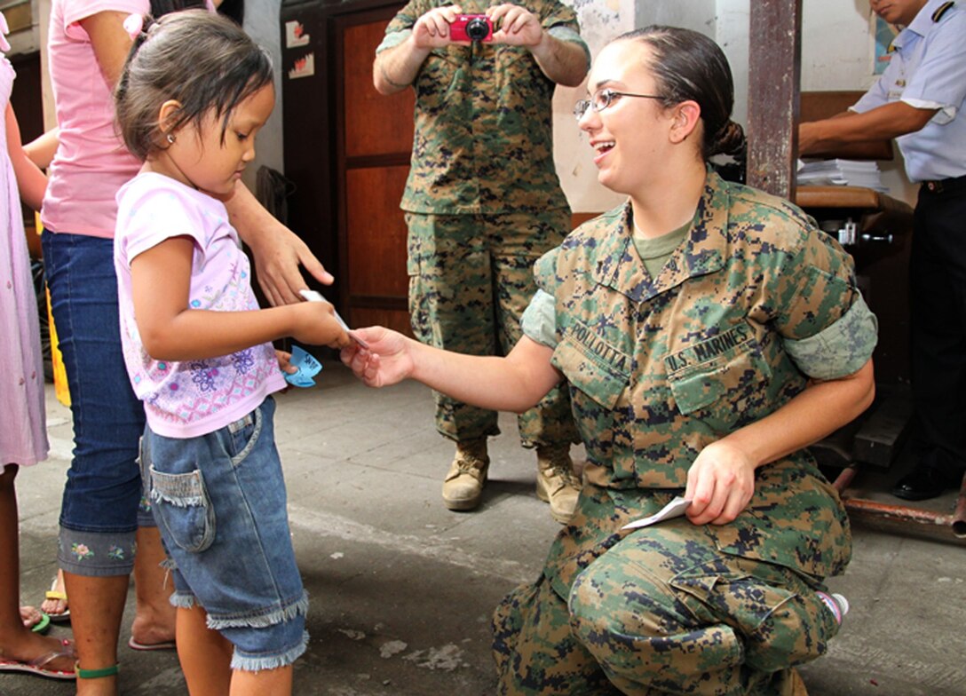 U.S. Marine Lance Cpl. Alycia Pollotta, intelligence analyst, III Marine Expeditionary Force, hands a Balikatan 2009 sticker to a Philippine girl during a civic military operation at the Santo Nino Parish Church here April 22. AFP and U.S. forces handed out more than a ton of clothing, toys and shoes to 200 needy families in the area on behalf of Operation Good Will. (Photo by Lance Cpl Cristina Gil)