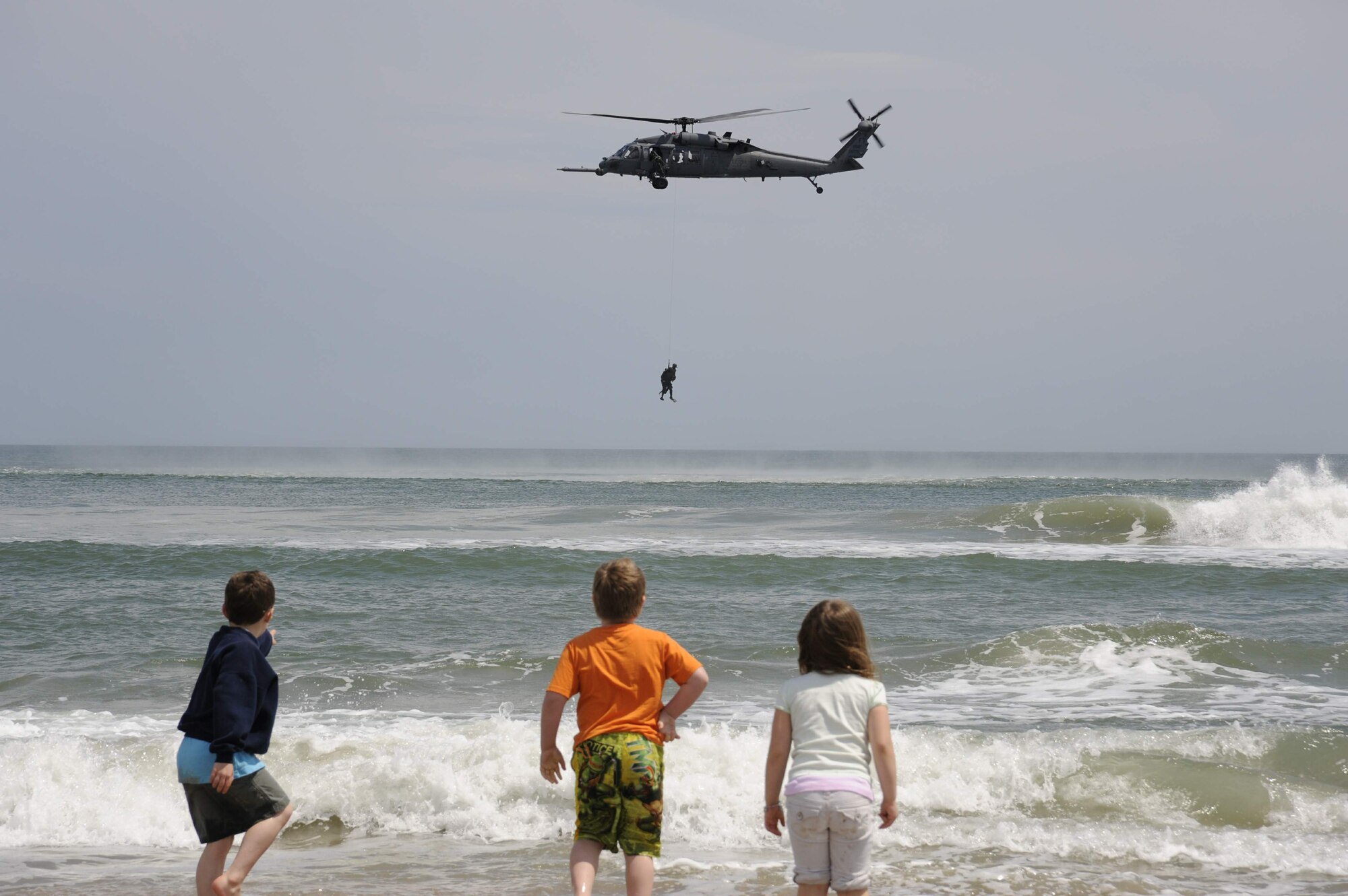 Michael Harris (left), Tyler Simmons and Elise Harris watch as a special forces team member gets reeled into an HH-60 Pave Hawk helicopter during a joint airpower demonstration as part of Air Force Week April 22 along the coastline of Virginia Beach, Va.  (U.S. Air Force photo)
