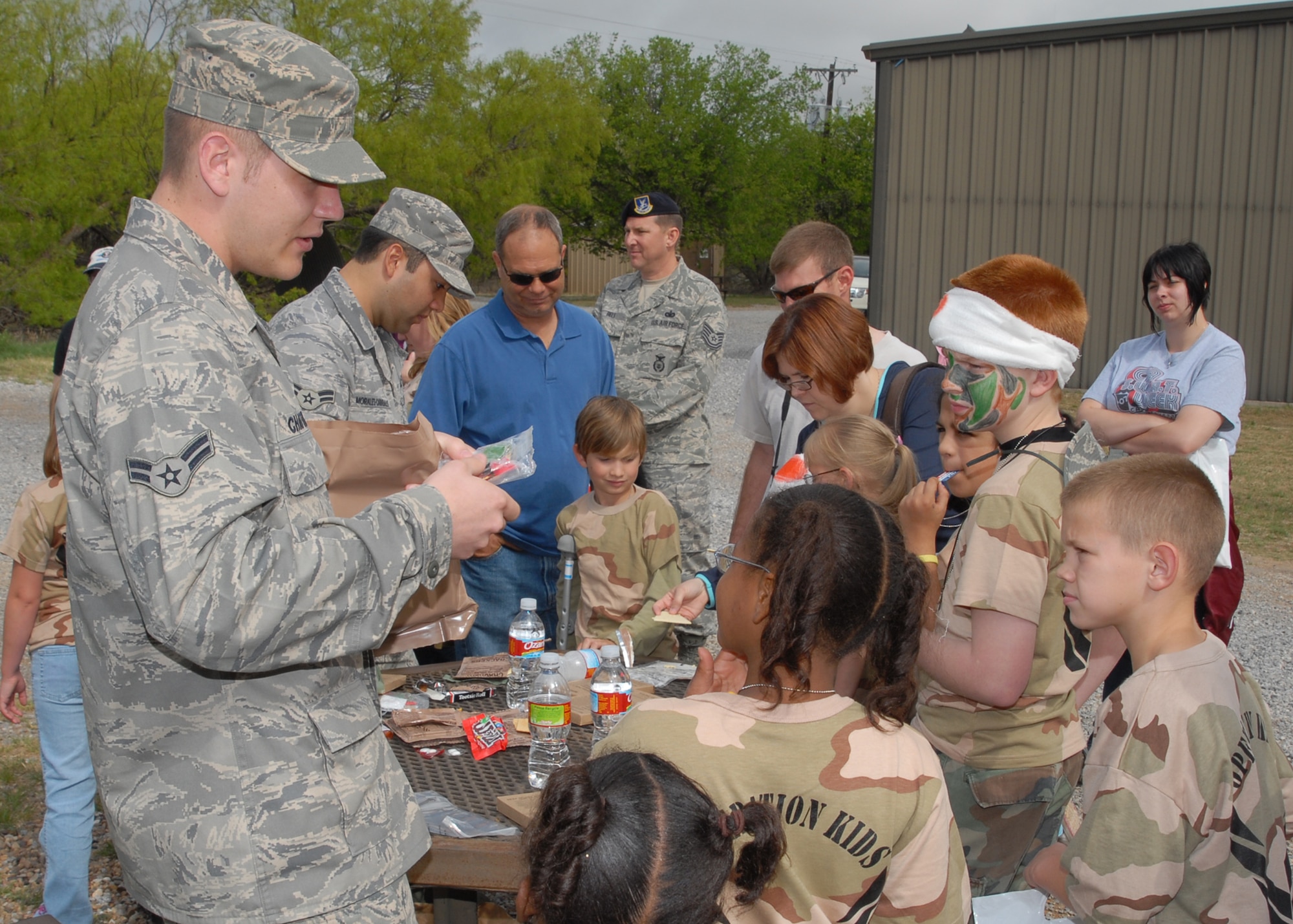 Airmen 1st Class David Chattin and Carlos Morales demonstrate the correct use of Meals, Ready to Eat at Operation KIDS April 18 at the Medical Readiness Site. 