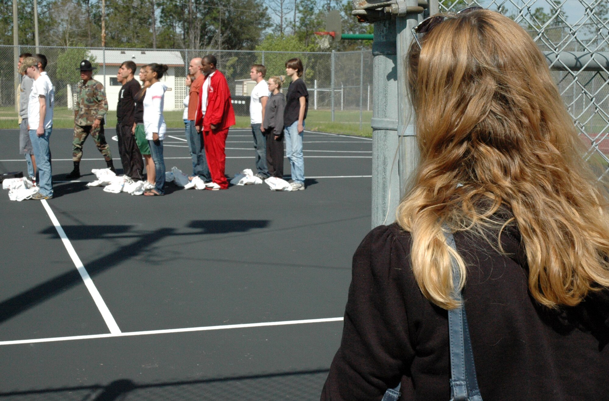 A mother stands outside the gate surrounding the volleyball court at Duke Field as her son, a recruit participating in the delayed entry program, receives instruction on military bearing and the position of attention from Senior Master Sgt. Steve Betancourt, 96th Medical Squadron, Eglin Air Force Base. Sergeant Betancourt, a former military training instructor of four years now assigned at Eglin AFB, volunteered during the April unit training assembly to give DEP recruits a taste of what they will experience upon arriving at basic military training, Lackland Air Force Base, Texas. The DEP maintains contact with recruits awaiting their ship date to BMT while ensuring they are in compliance with the Air Force Reserve standards. It also gives recruits the information and motivation to have a smoother transition from civilian to military life. (U.S. Air Force photo /Senior Airman Jon McCallum)