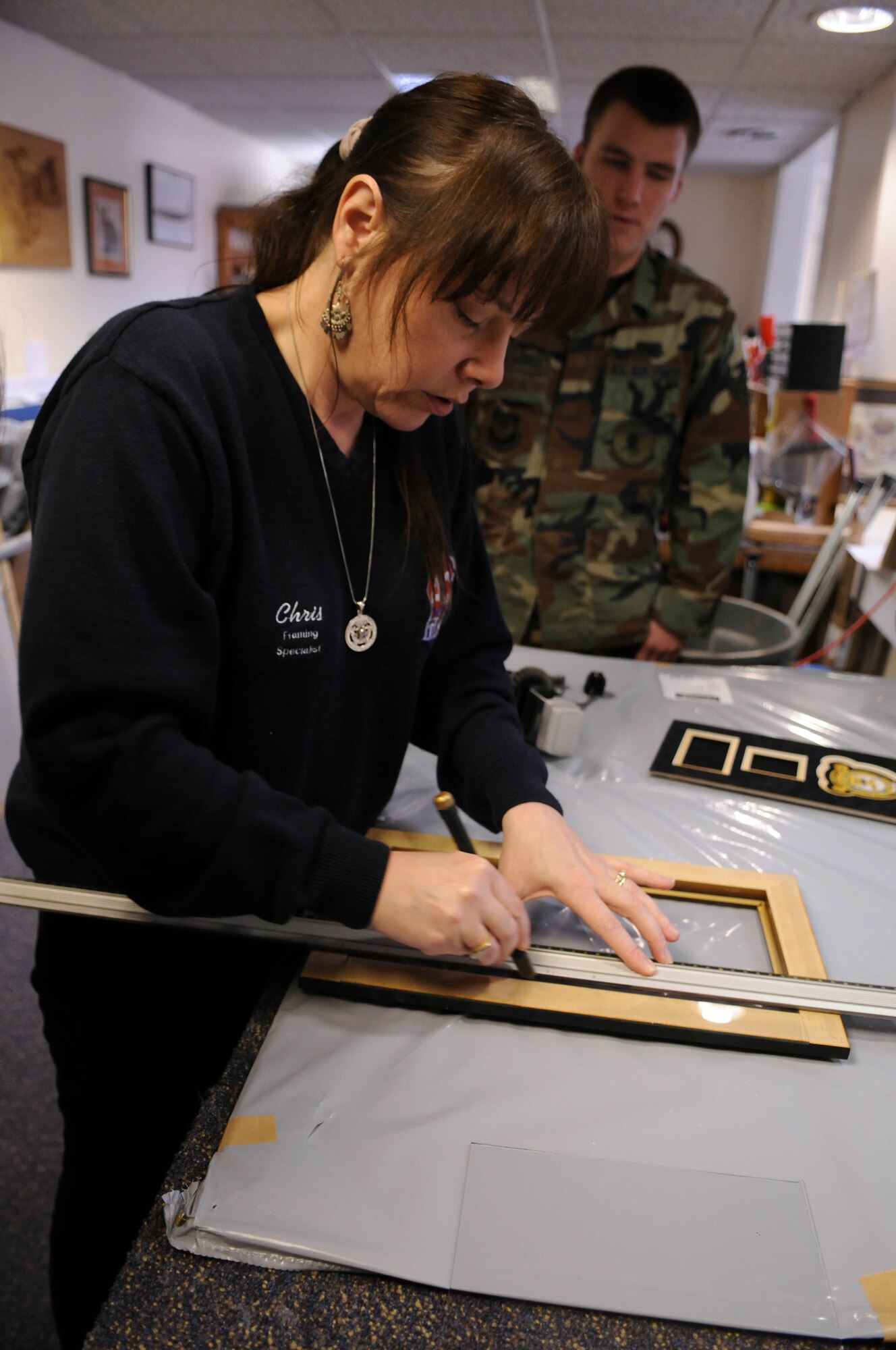 Chris Acker, 100th Force Support Squadron professional framer, cuts a piece of glass to be put into a frame she is building for a customer.  Mrs. Acker, who has been framing for more than a decade, uses a mixture of automated equipment and precision hand tools to create her works of art each day at the RAF Mildenhall frame shop.  (U.S. Air Force photo by Staff Sgt. Austin M. May)