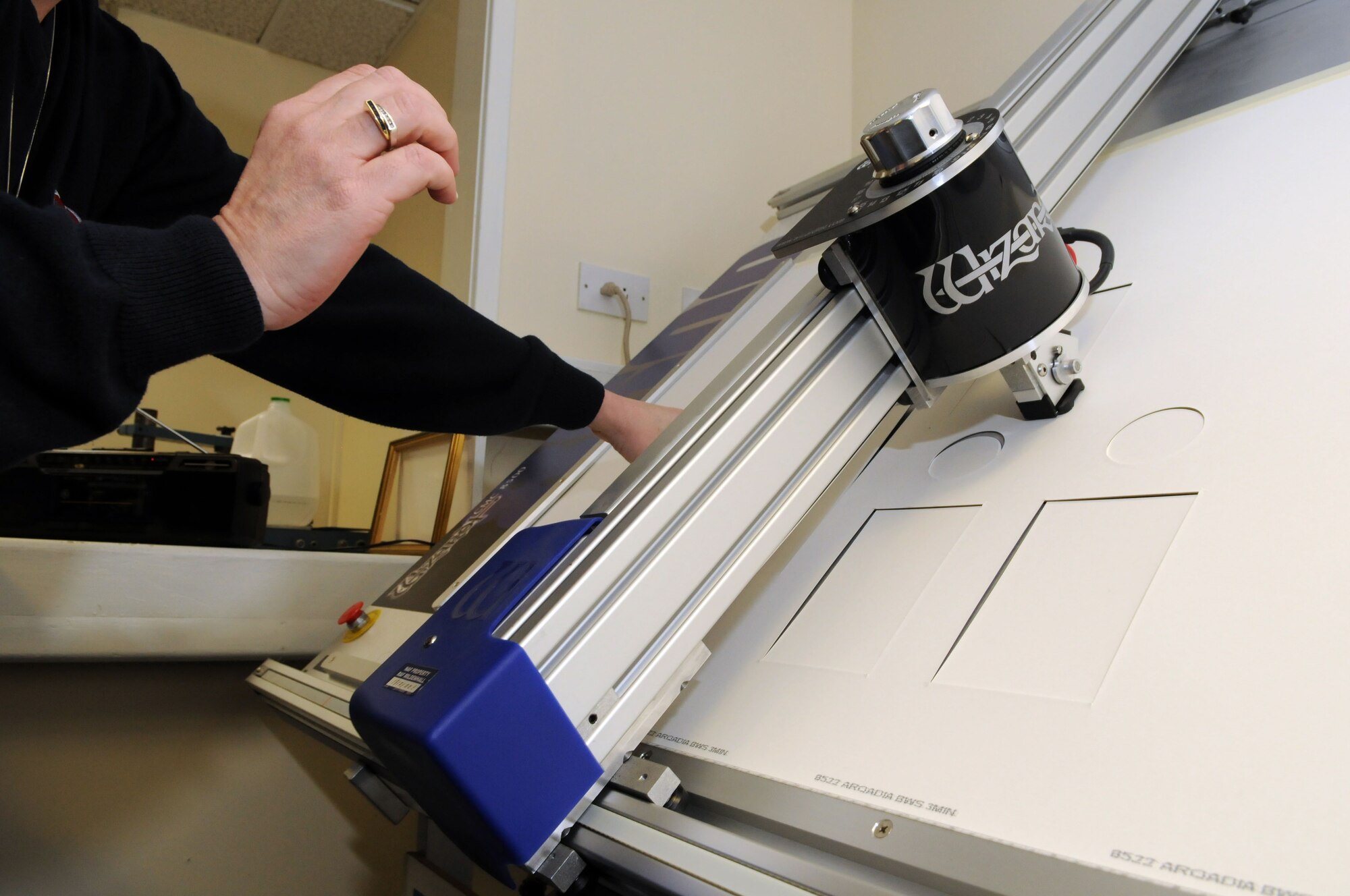 Chris Acker, 100th Force Support Squadron professional framer, keeps pressure on a mat being cut by the RAF Mildenhall frame shop’s automated mat cutter.  The high-tech cutter makes very fine details easy to incorporate into picture framing projects, and makes simple mats quick and easy to create.  (U.S. Air Force photo by Staff Sgt. Austin M. May)