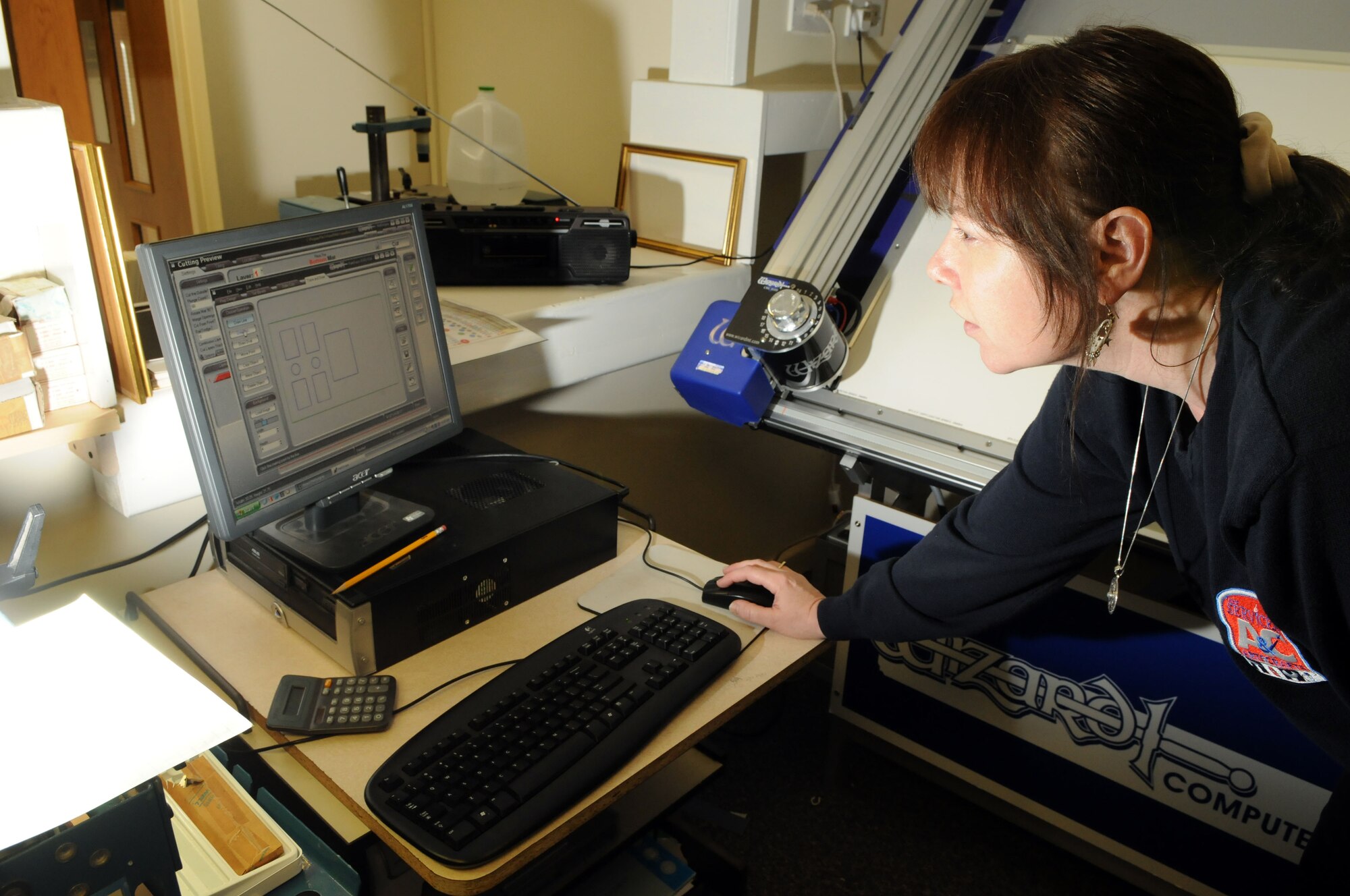 Chris Acker, 100th Force Support Squadron professional framer, inputs a design into the RAF Mildenhall frame shop’s automated mat cutter.  The high-tech cutter makes very fine details easy to incorporate into framing projects.  (U.S. Air Force photo by Staff Sgt. Austin M. May)